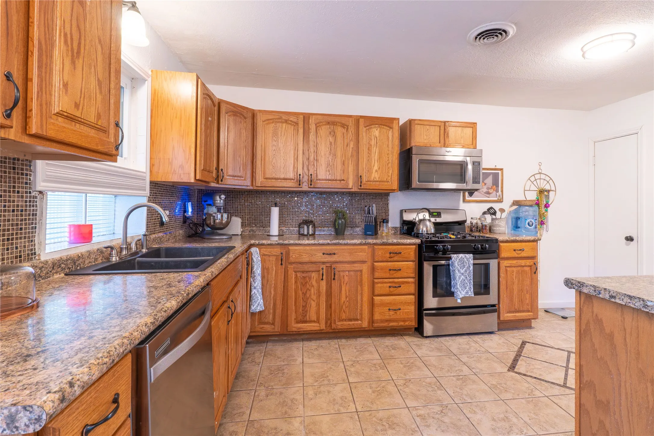 Kitchen with wood finish cabinetry, stainless steel appliances, light tile patterned floors, and backsplash