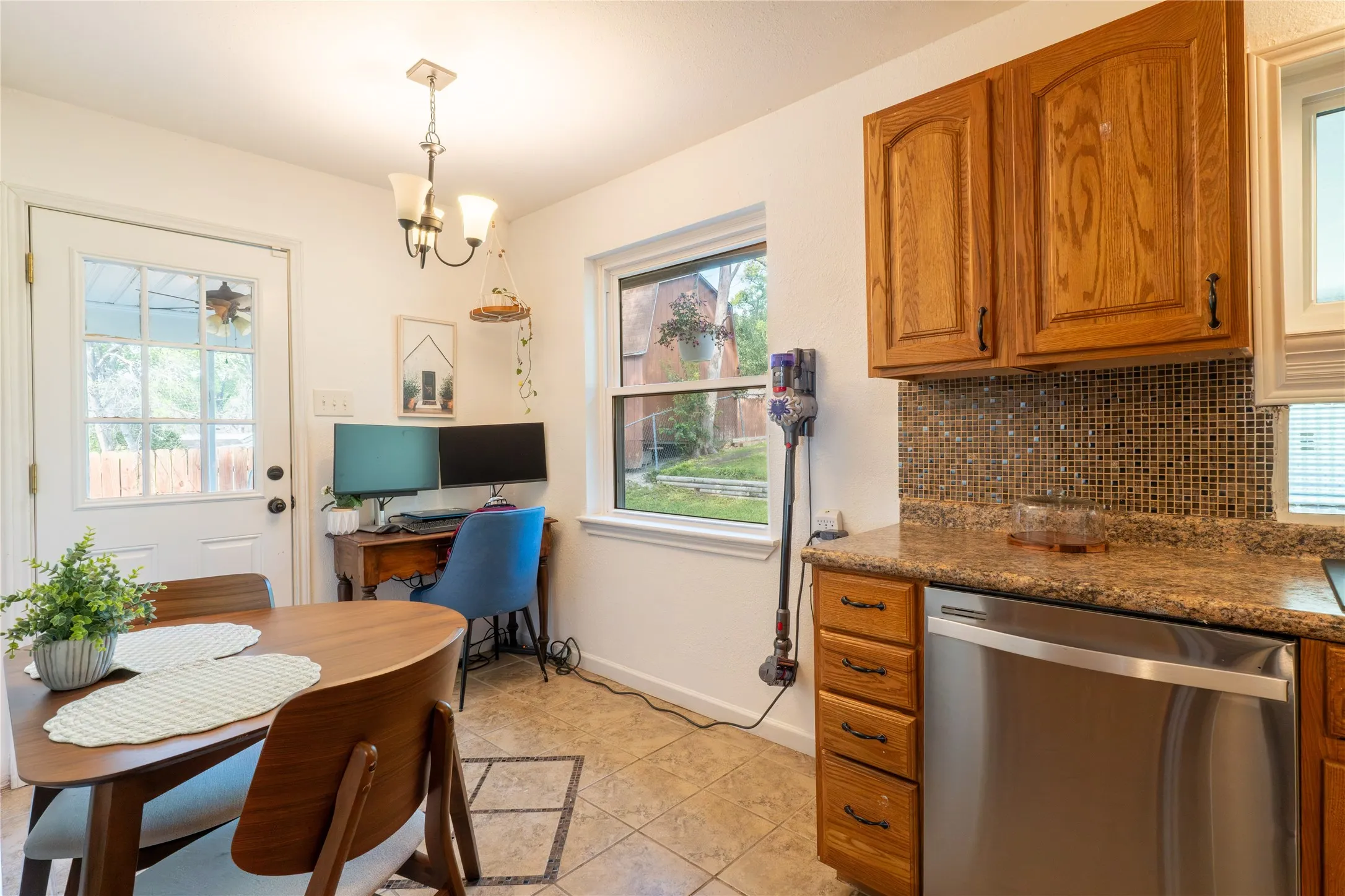 Kitchen with wood finish cabinetry, stainless steel dishwasher, dark stone counters, a chandelier, and light tile patterned flooring
