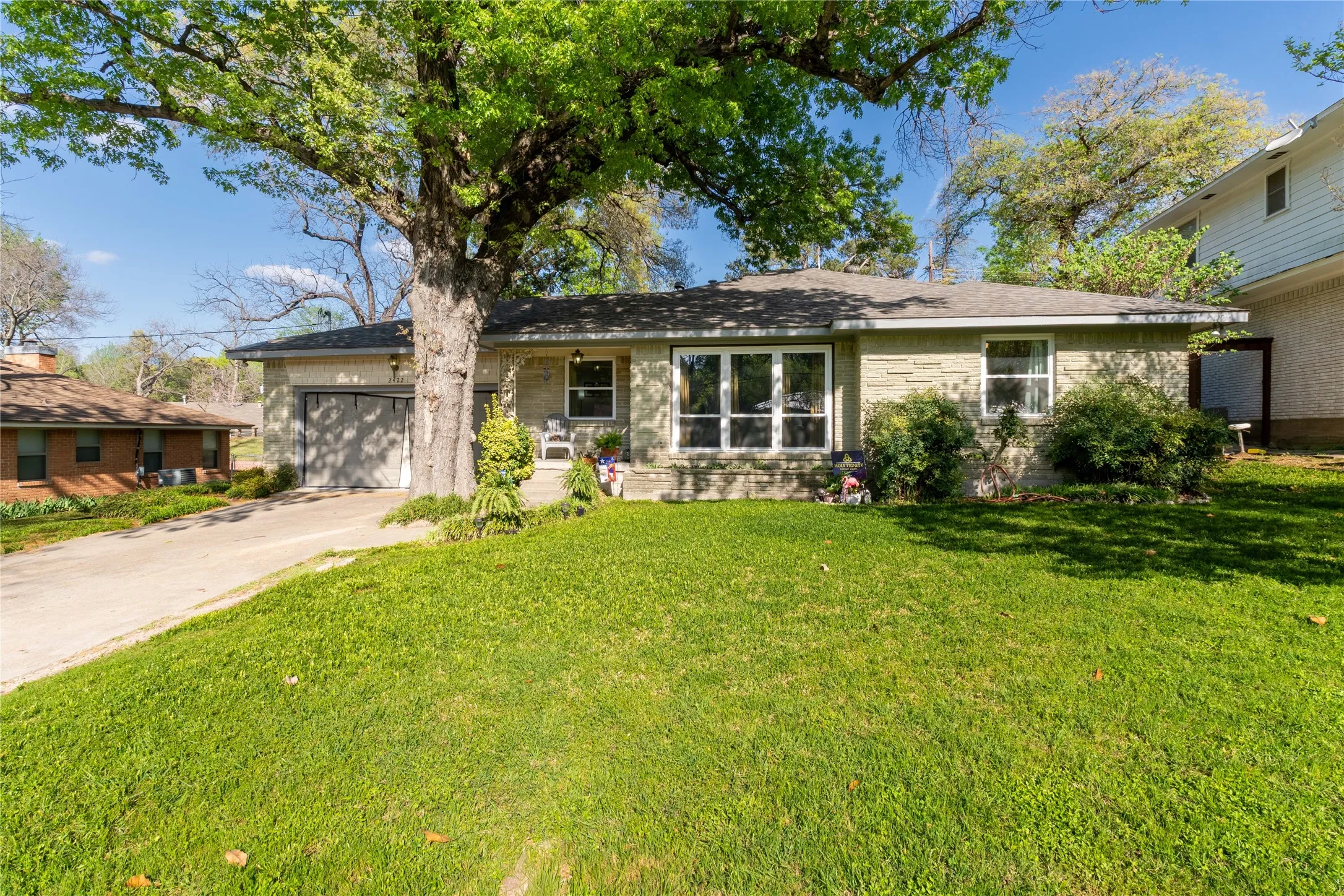 Single story home with a garage, driveway, a front lawn, and brick siding
