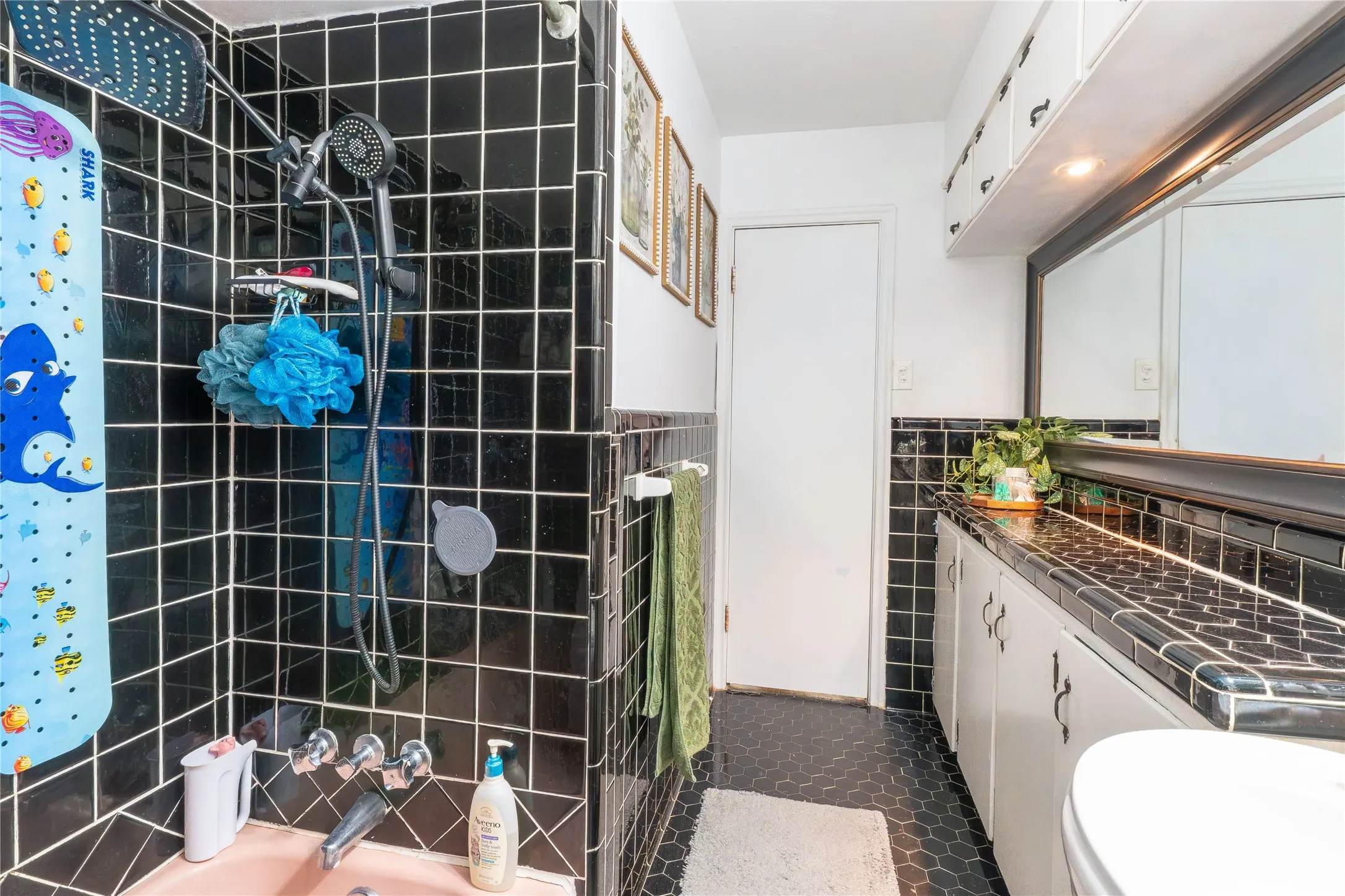 Bathroom featuring tile walls, vanity, dark tile patterned floors, tiled shower / bath combo, and wainscoting