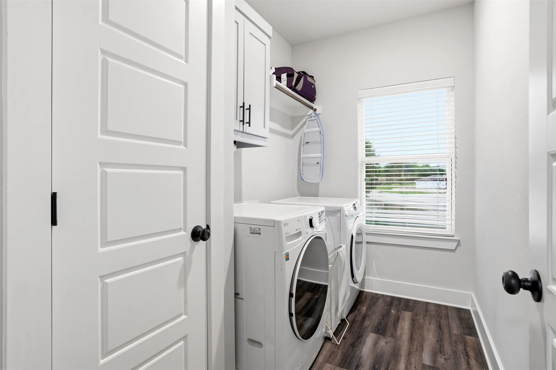 Laundry area featuring dark wood finished floors, washing machine and clothes dryer, and cabinet space