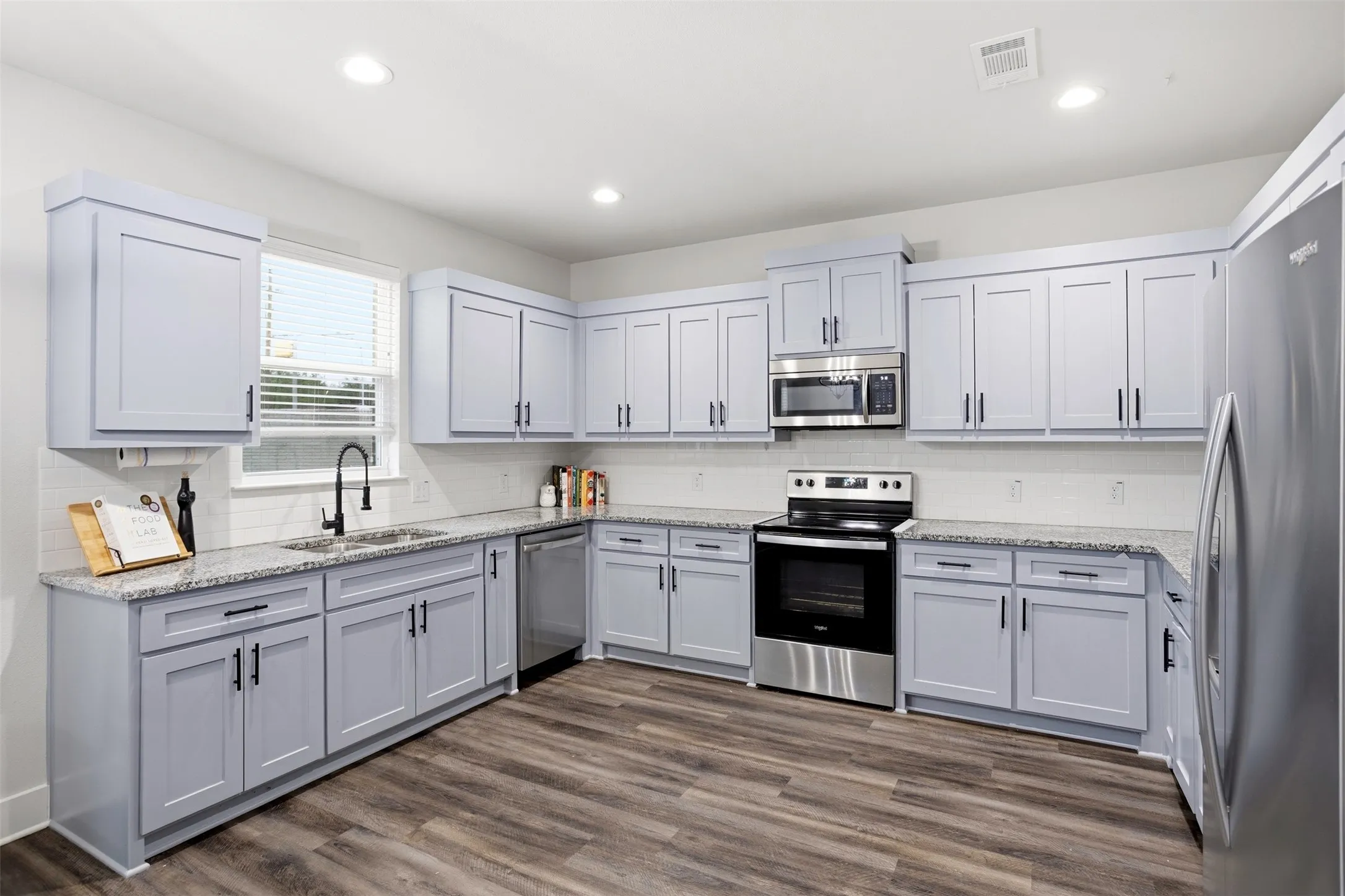Kitchen featuring stainless steel appliances, light stone countertops, decorative backsplash, dark wood-style flooring, and recessed lighting