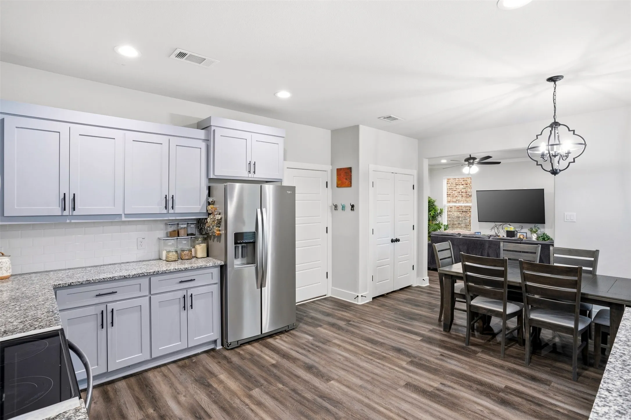 Kitchen featuring stainless steel fridge with ice dispenser, suspended lighting, black electric range, dark wood-style flooring, and light stone counters