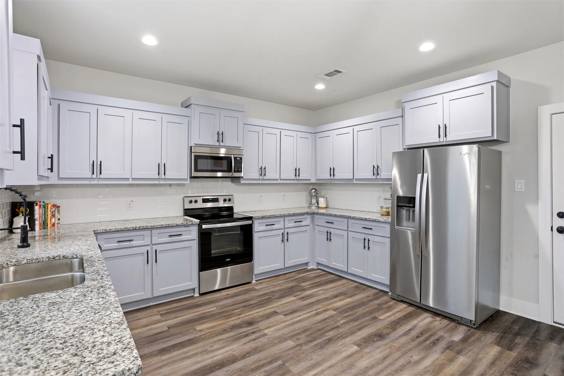 Kitchen with stainless steel appliances, light stone counters, dark wood finished floors, decorative backsplash, and recessed lighting