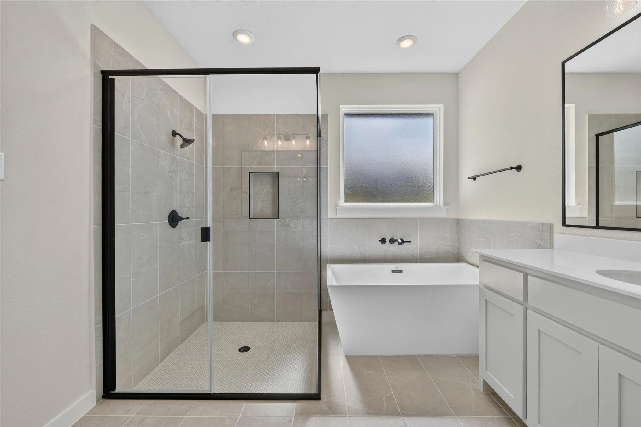 Contemporary bathroom featuring a spacious walk-in shower with black-framed glass enclosure, a freestanding soaking tub, dual vanity with white cabinetry and countertops, and modern matte black fixtures