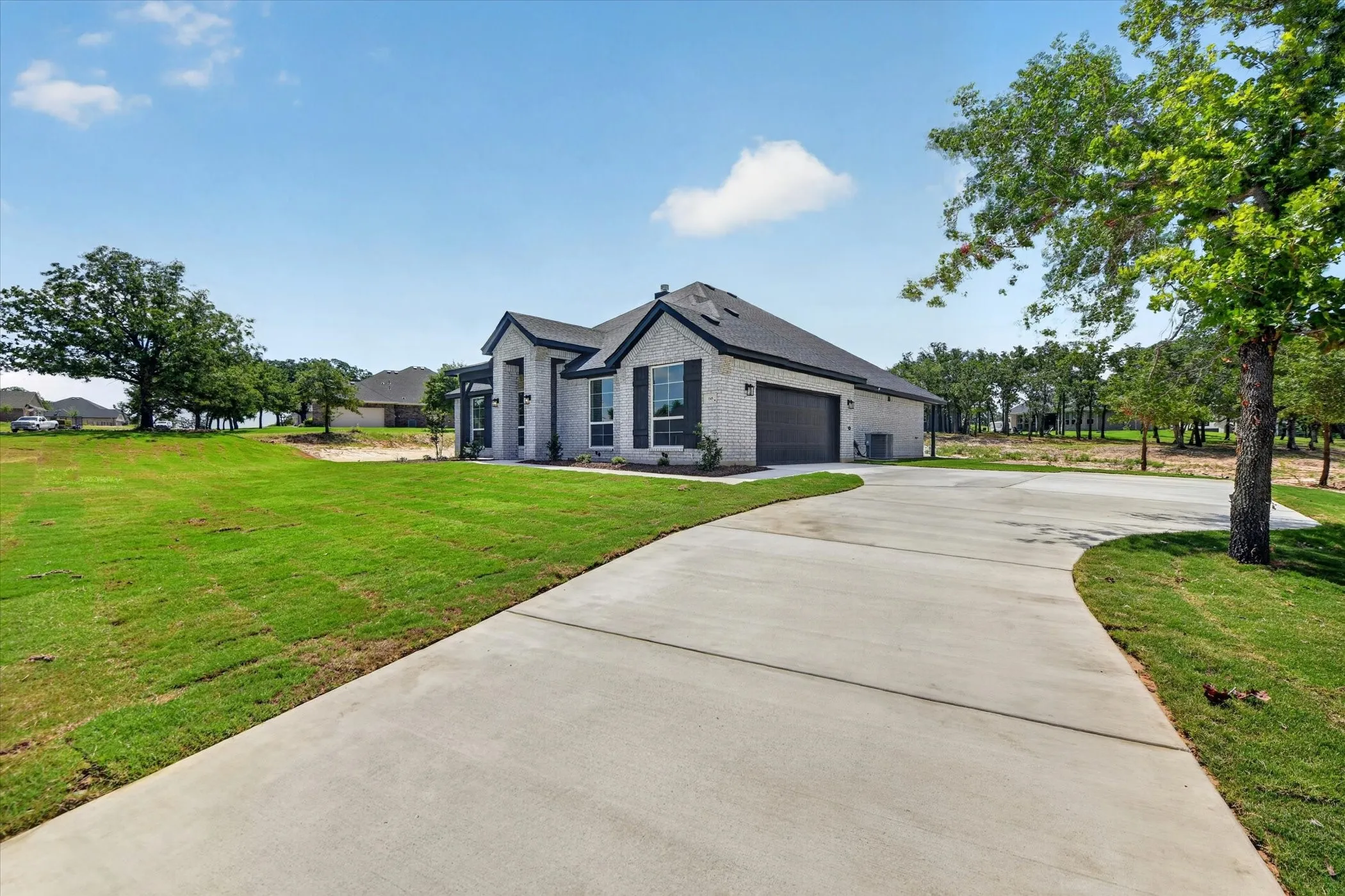 Contemporary-style home featuring a light-colored brick exterior, dark-trimmed windows with shutters, and a dark shingle roof