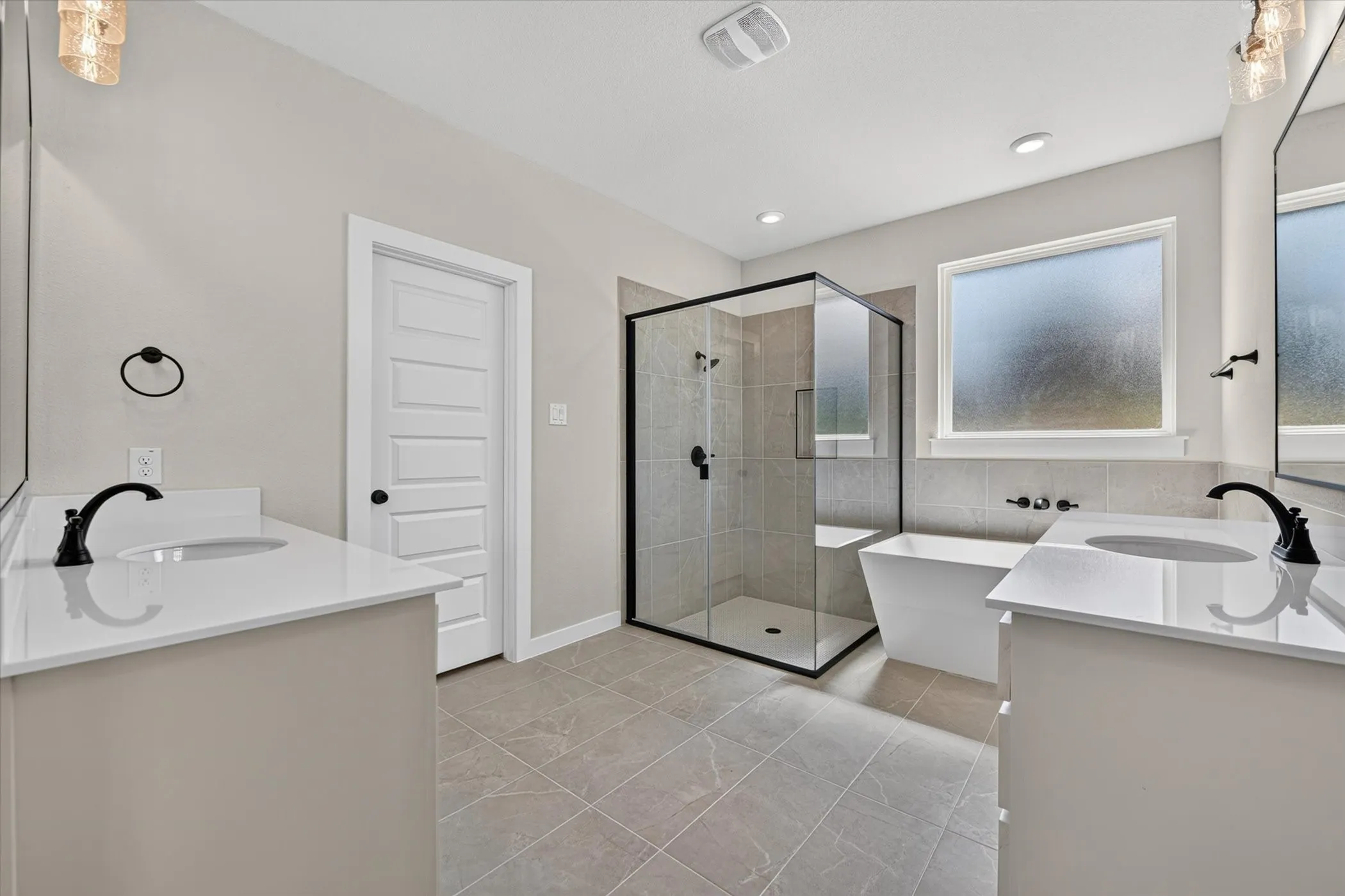 Bathroom featuring a glass-enclosed shower, freestanding tub, dual vanity with quartz countertops, and matte black fixtures