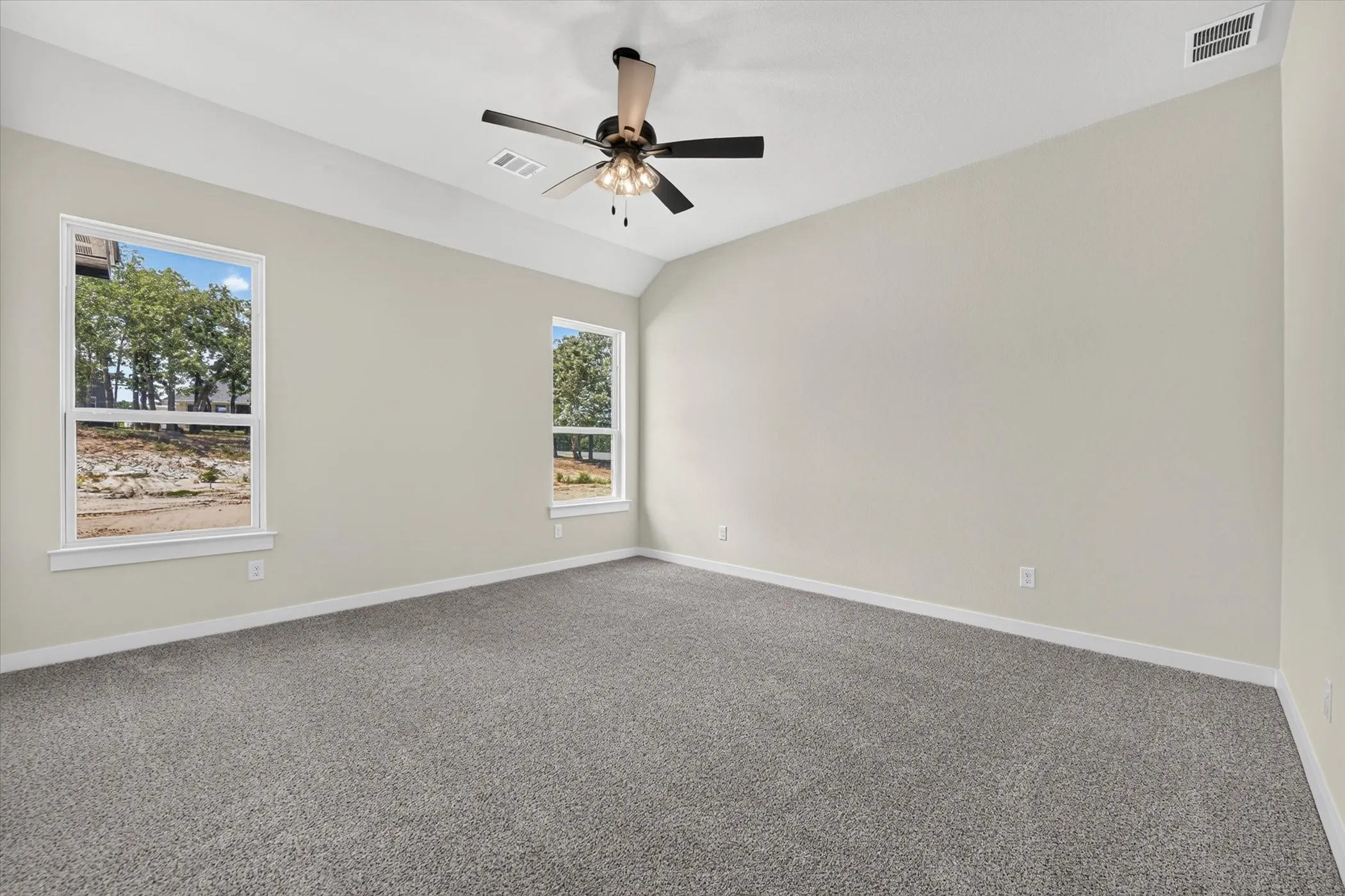 Spacious room featuring vaulted ceilings, two large windows, a ceiling fan with integrated lighting, neutral wall tones, and plush carpeting