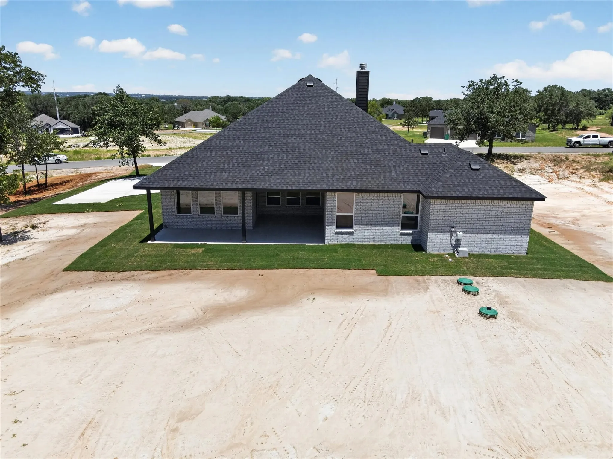 Rear exterior featuring light grey brick, a dark shingle roof, and a covered concrete patio