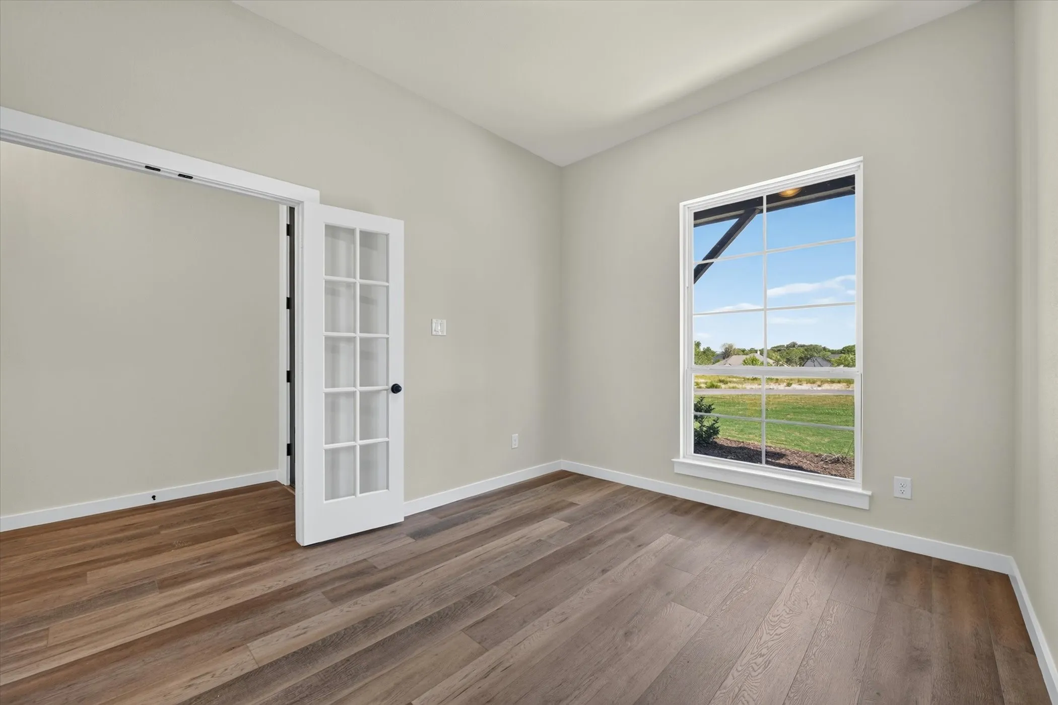 Bright interior room featuring wood-finish flooring, white baseboards, and a large window with white framing