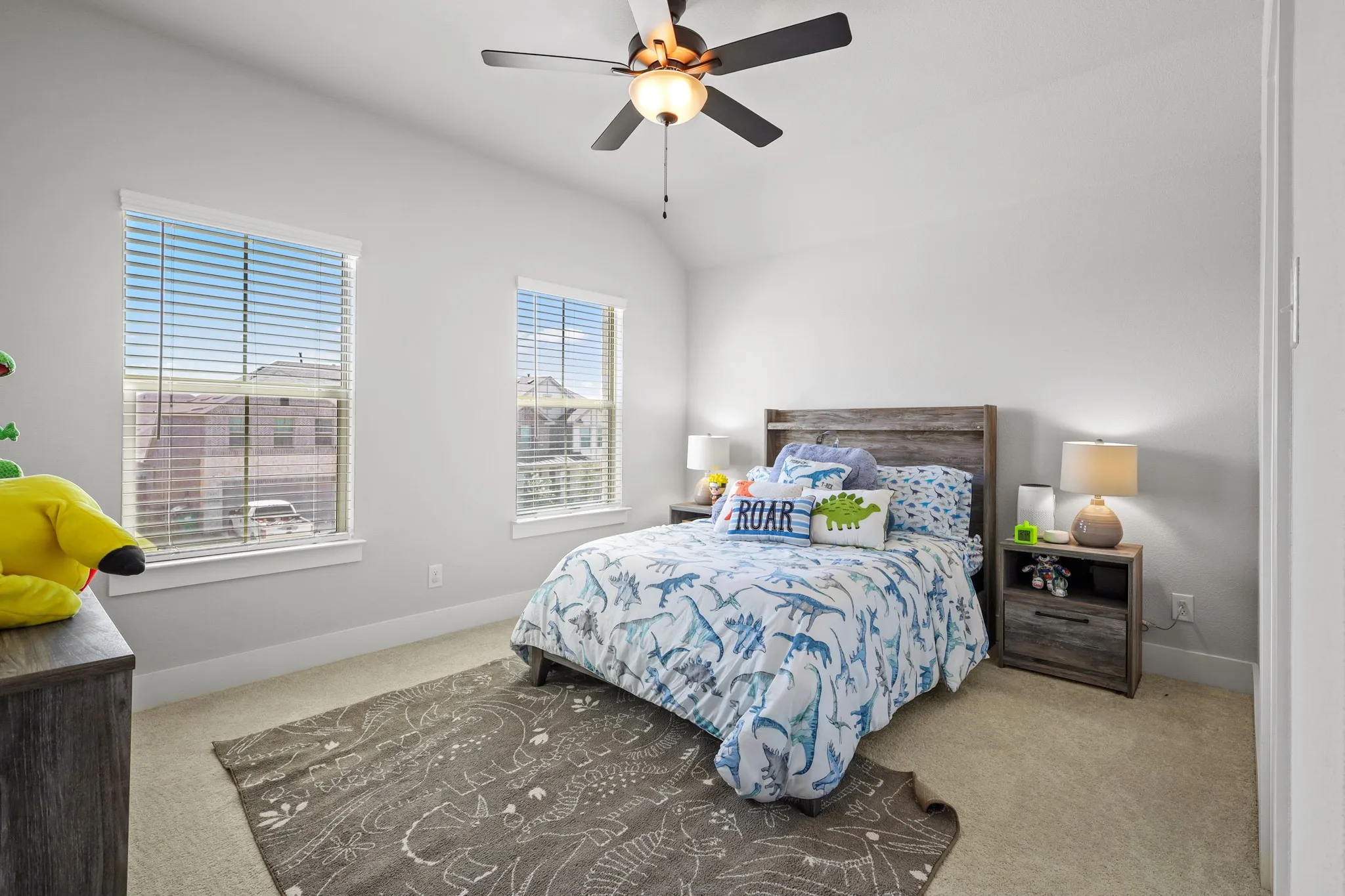 Carpeted bedroom with ceiling fan, multiple windows, and lofted ceiling