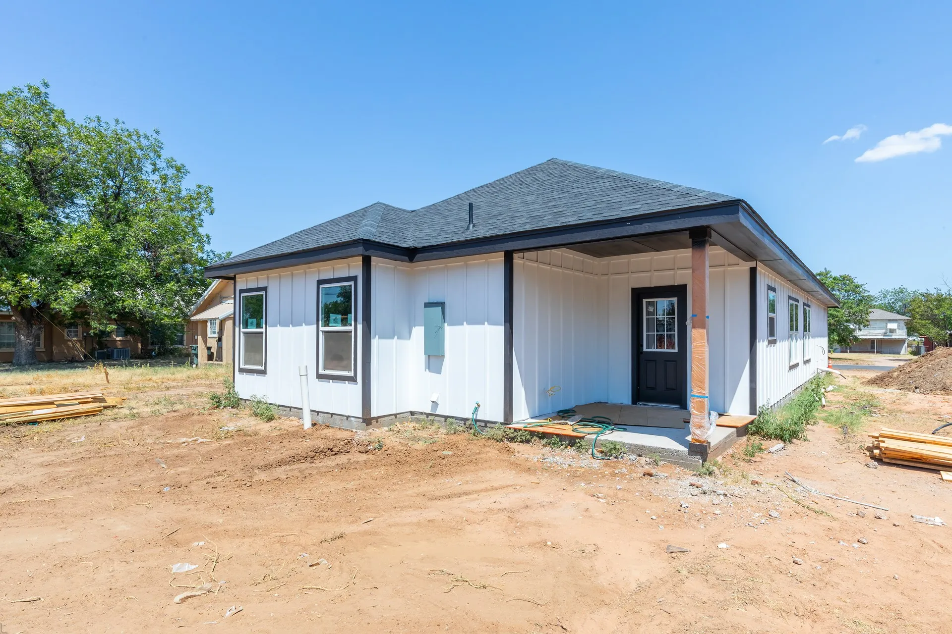 Modern single-story residence featuring a clean white exterior with dark roof accents, covered front porch with support columns, and multiple window openings providing natural light