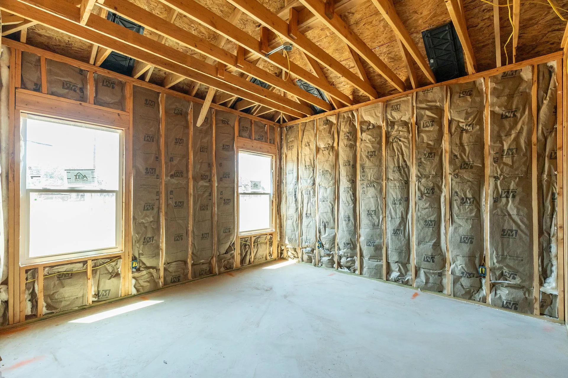 Exposed wood framing, two windows, insulated wall cavities, engineered wood roof sheathing, and concrete subfloor