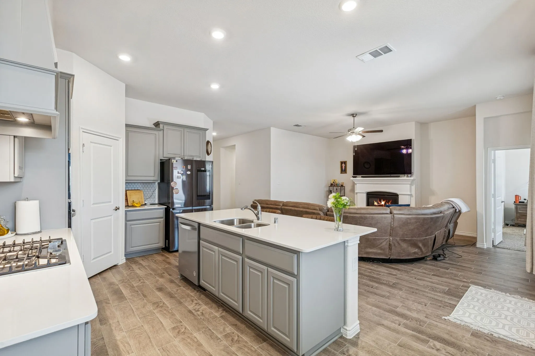 Kitchen featuring gray cabinets, a lit fireplace, wood tiled floors, open floor plan, and an island with sink