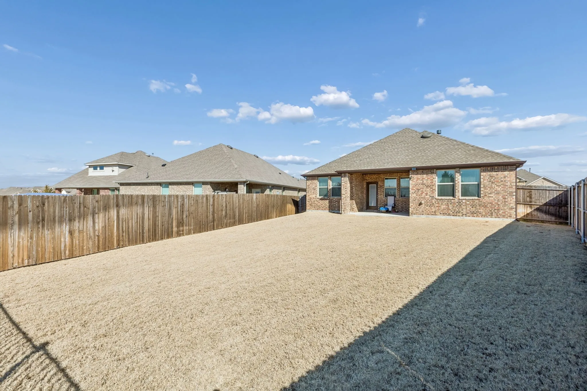 Back of house featuring brick siding, a fenced backyard, a patio area, and roof with shingles