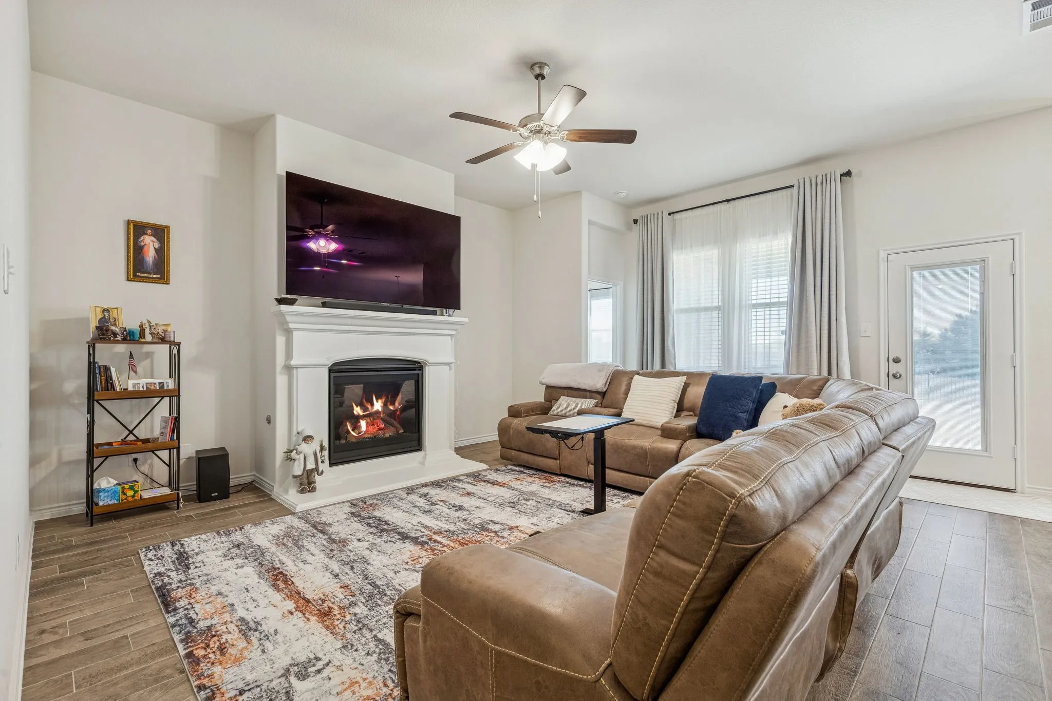Living area with wood tiled floors, a glass covered fireplace, and a ceiling fan