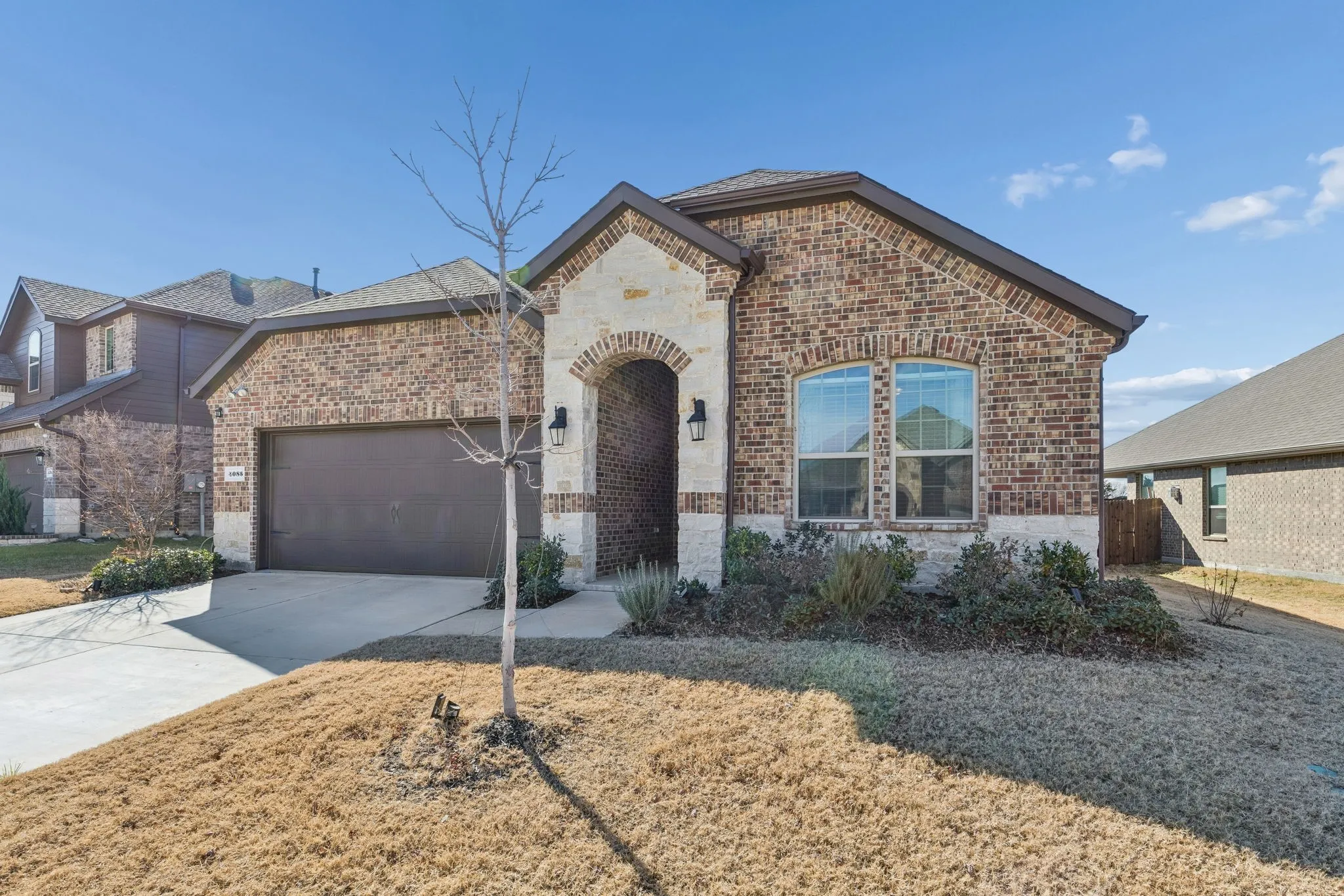 French country home featuring brick siding, an attached garage, driveway, and stone siding