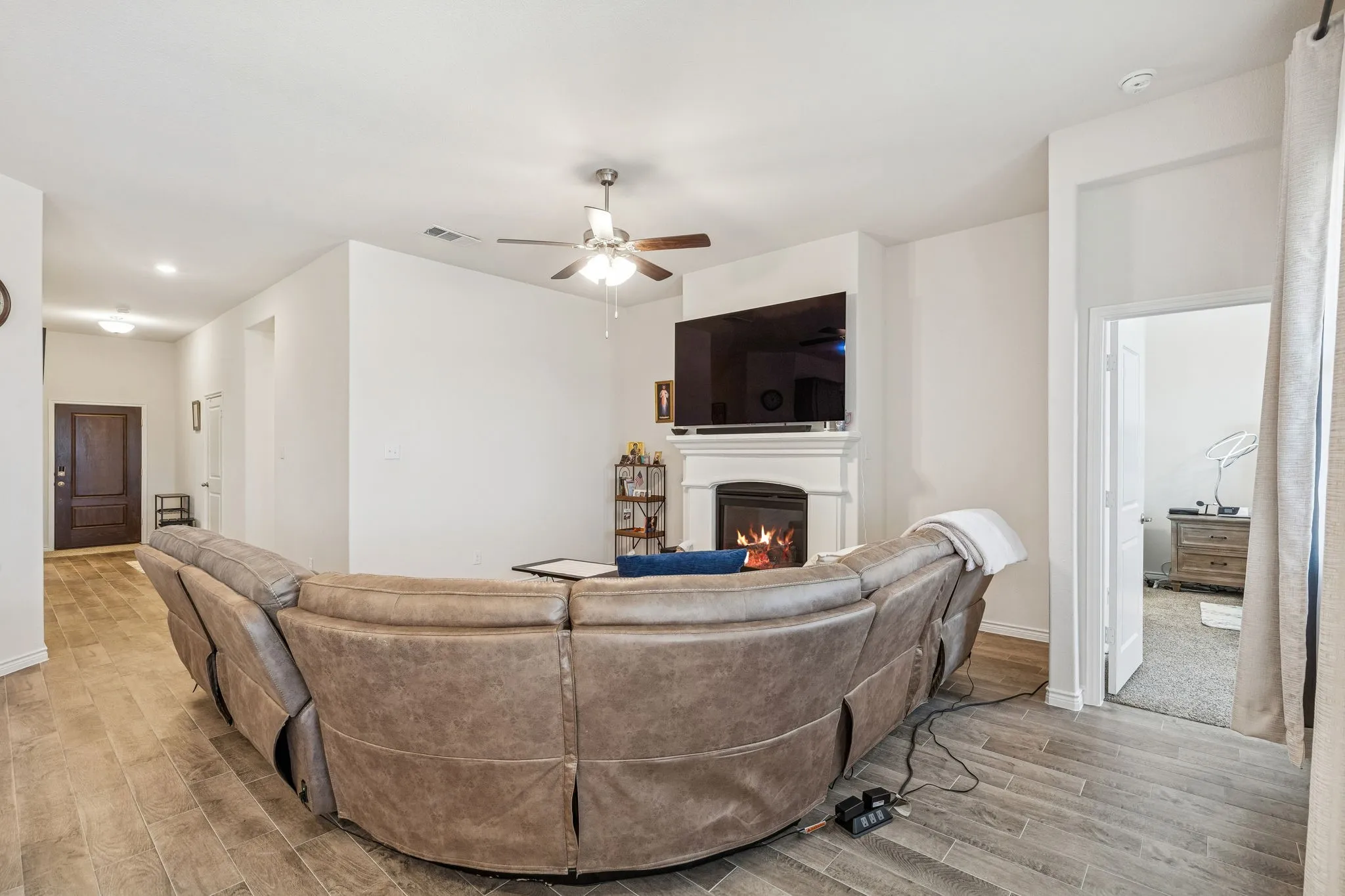 Living area featuring wood finish floors, a warm lit fireplace, and a ceiling fan