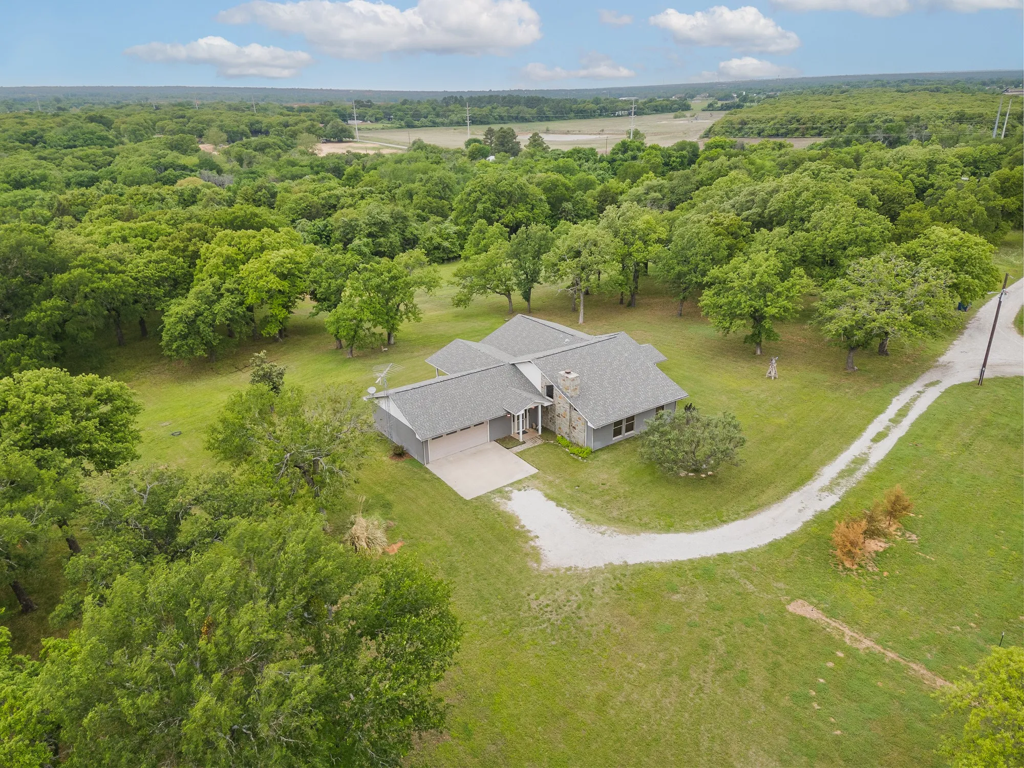 The property is nestled amidst extensive greenery, featuring a gray-roofed residence with a prominent stone chimney
