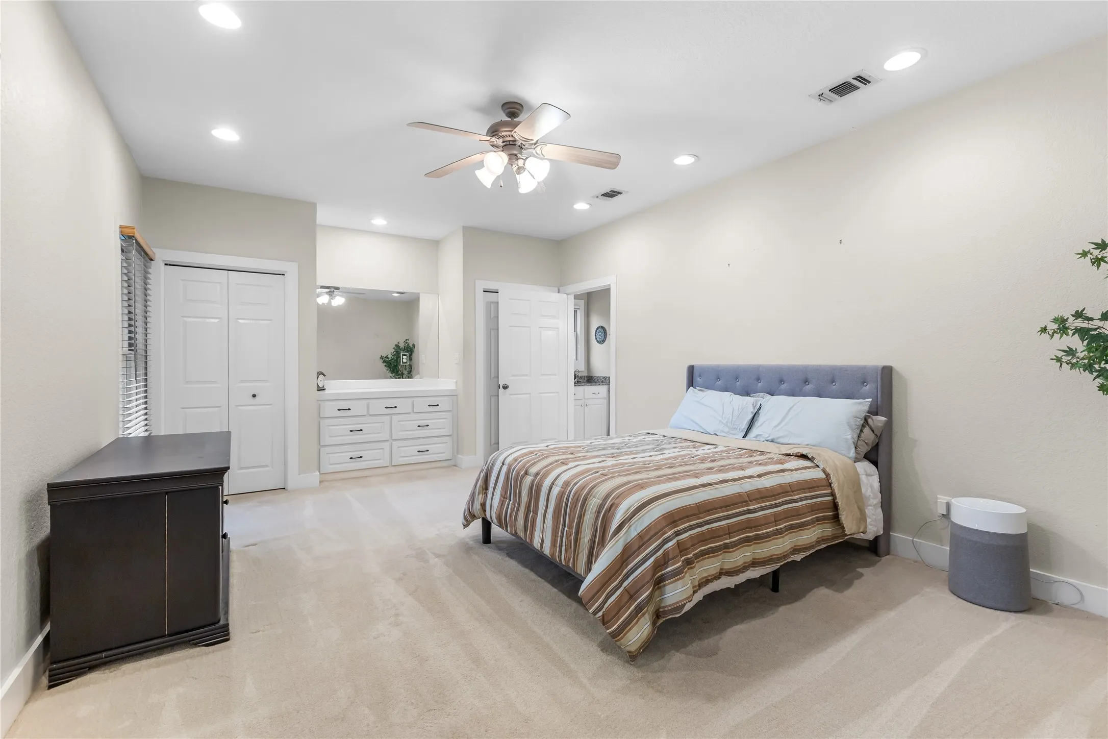 The property features a spacious room with light-colored carpet, recessed lighting, closets, built in dresser and a ceiling fan