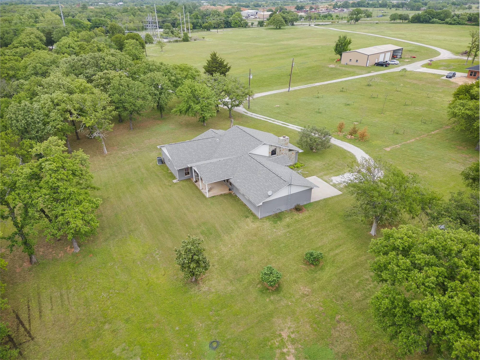 This property features a single-story residence with a gray roof and light-colored siding, set amidst expansive green lawns and mature trees
