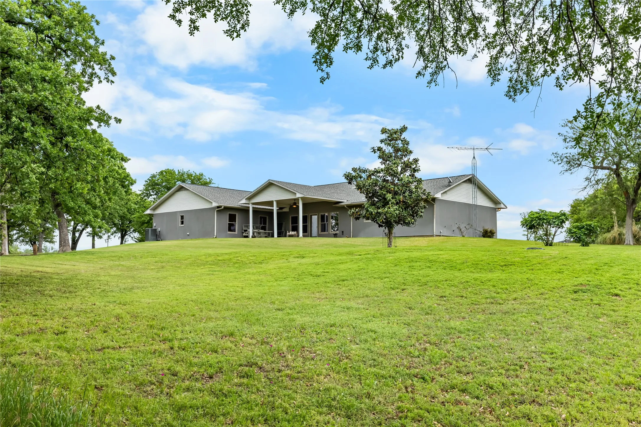 Expansive lawn surrounding the property with mature trees and a covered patio area