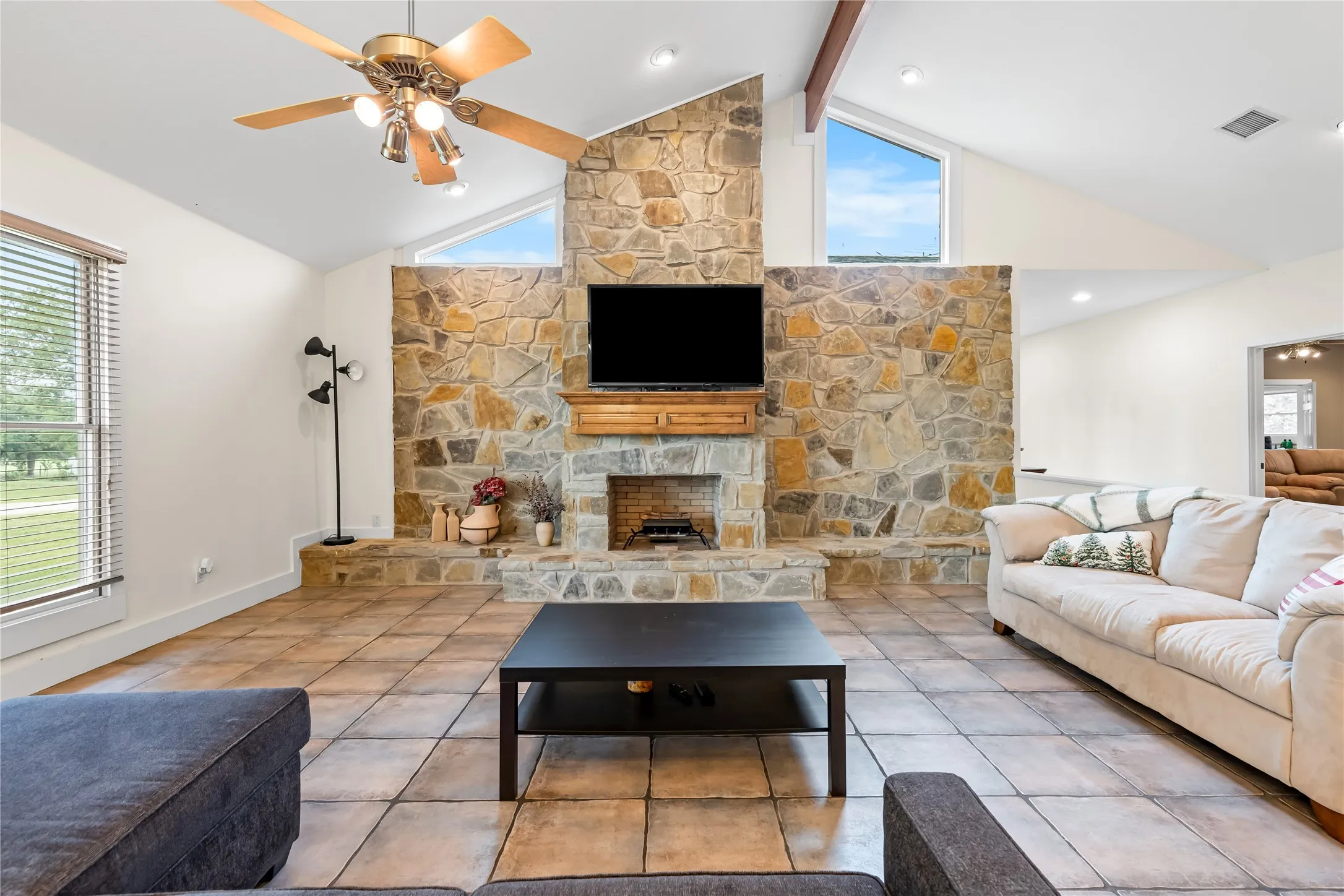 Spacious living area featuring a stone fireplace, vaulted ceilings, and large windows providing natural light