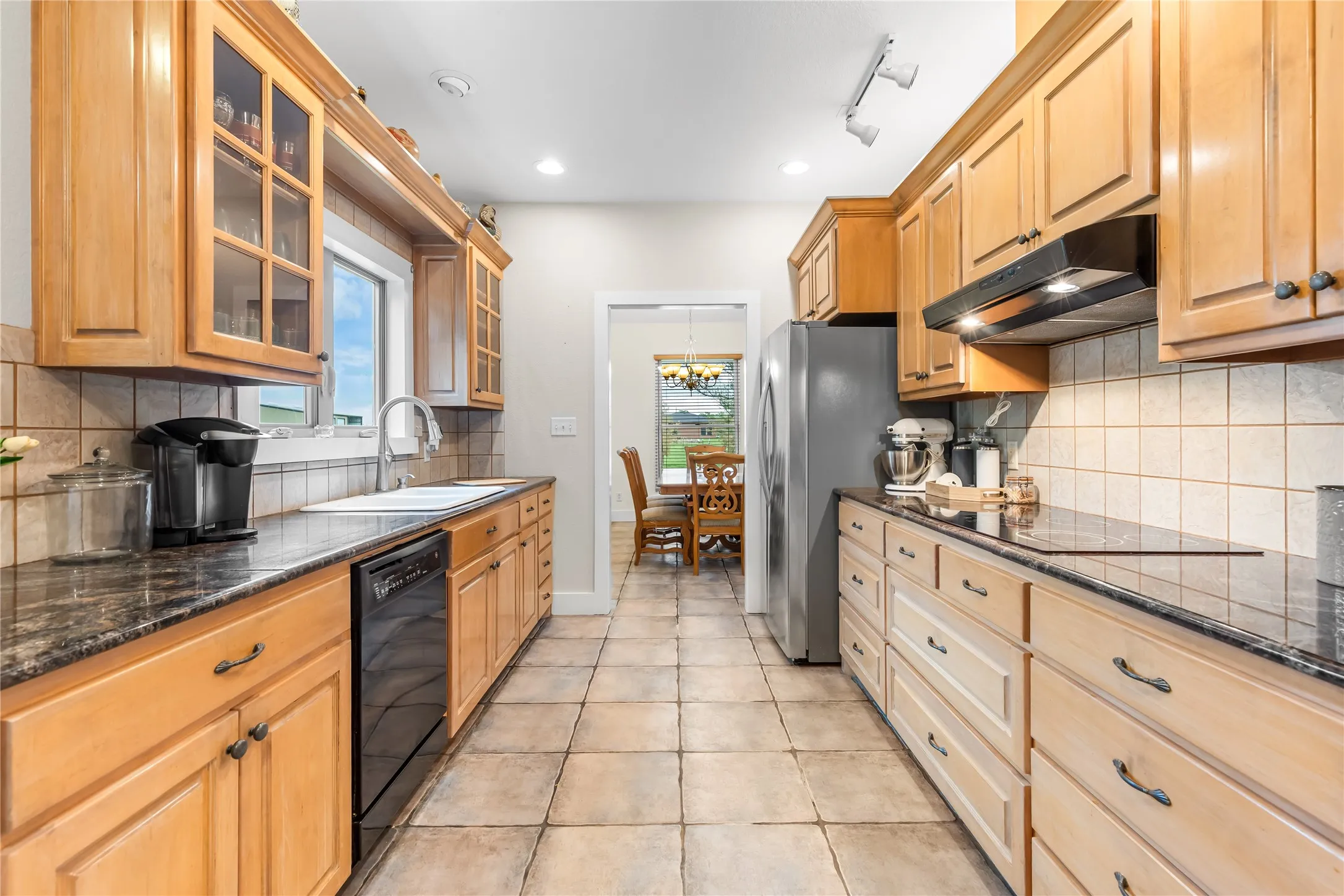 The kitchen features light wood cabinetry, dark countertops, and tile flooring