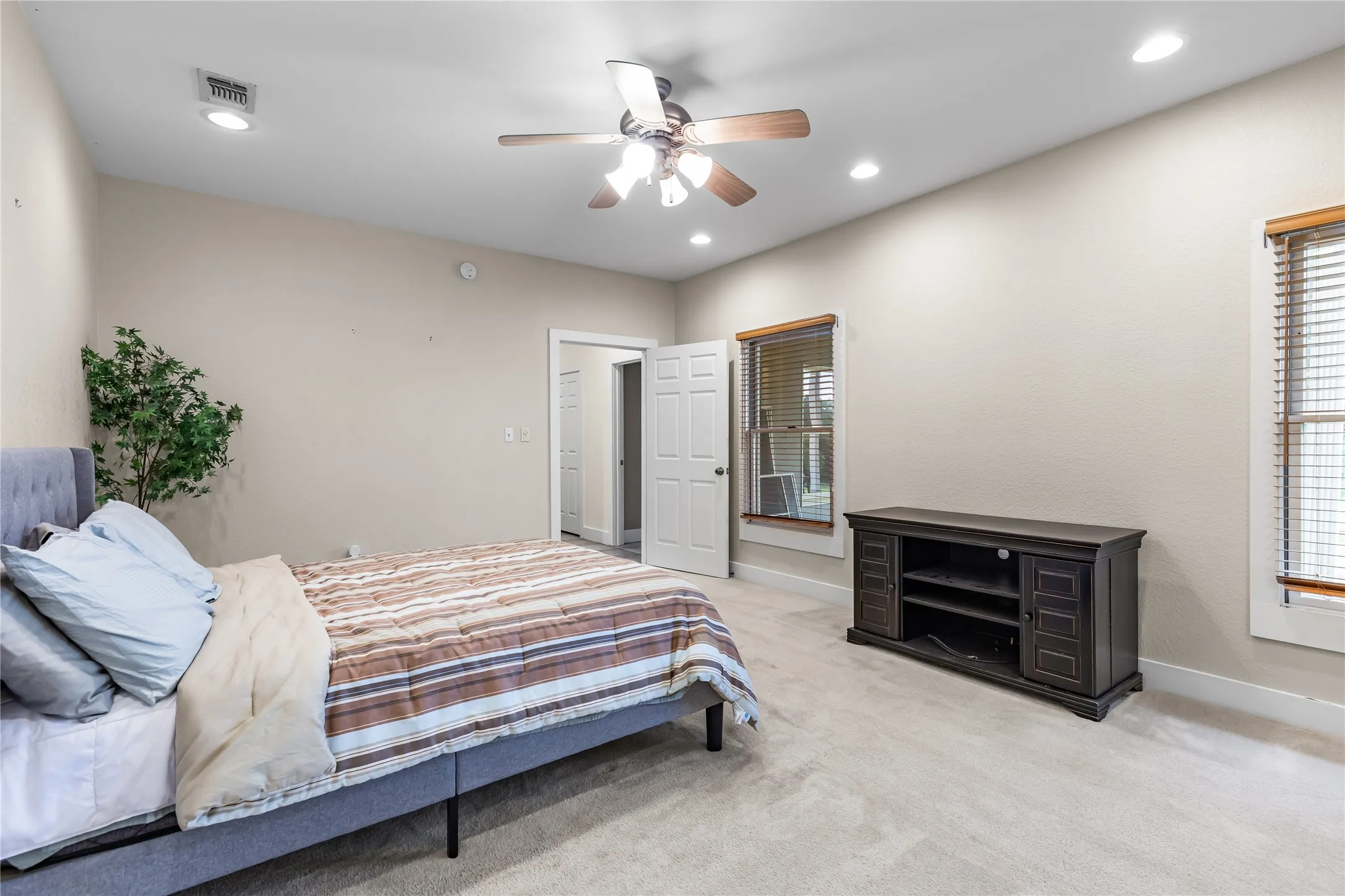 Bedroom featuring carpeted flooring, two windows with wooden blinds and trim, and a ceiling fan with integrated lighting