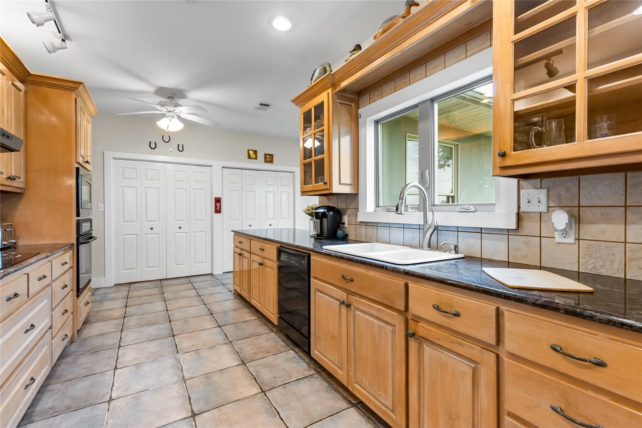 The kitchen features light wood cabinetry, dark countertops, and a tiled floor