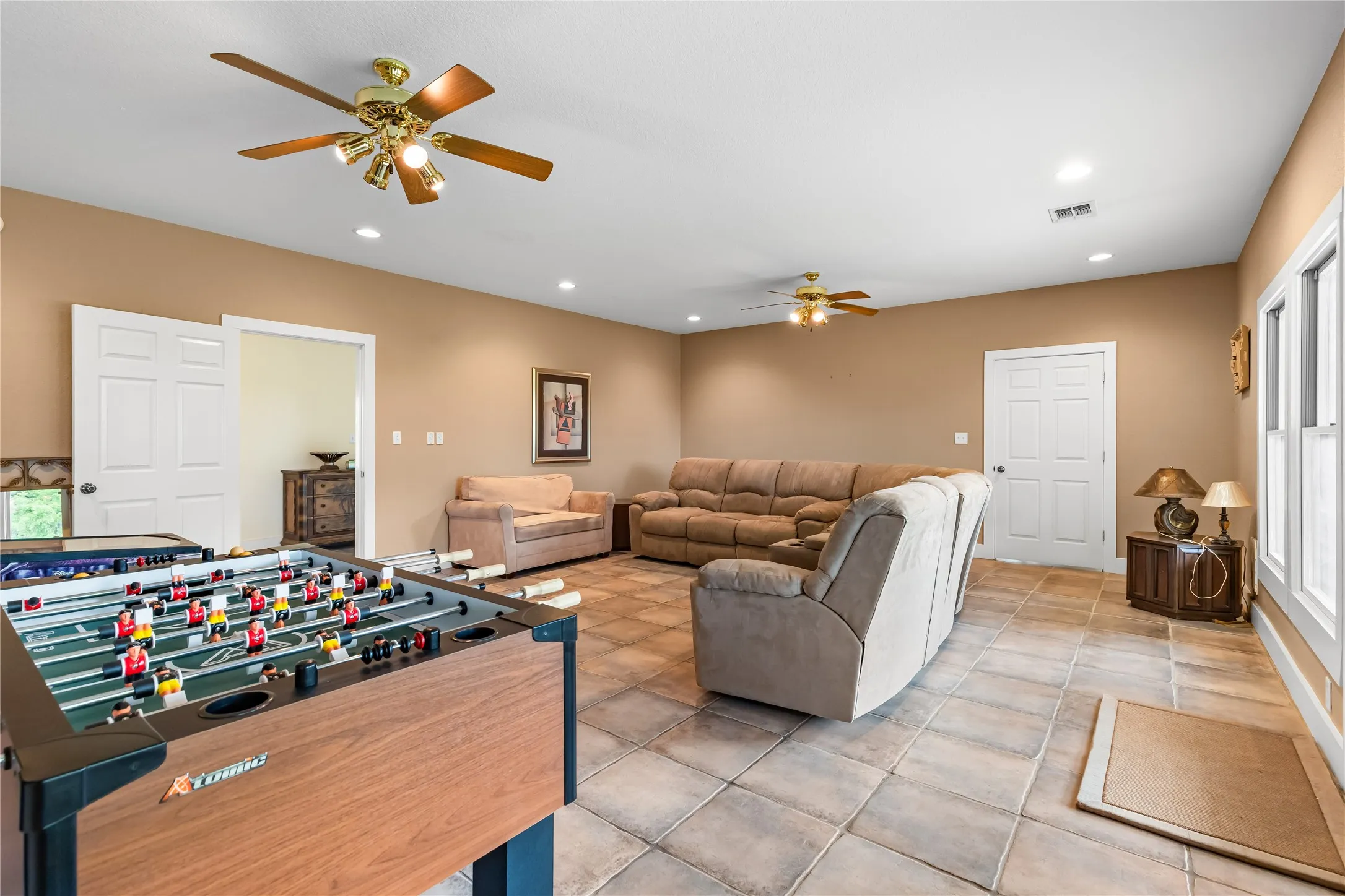 Spacious room featuring tile flooring, ceiling fans, recessed lighting, and white trim around windows and doors