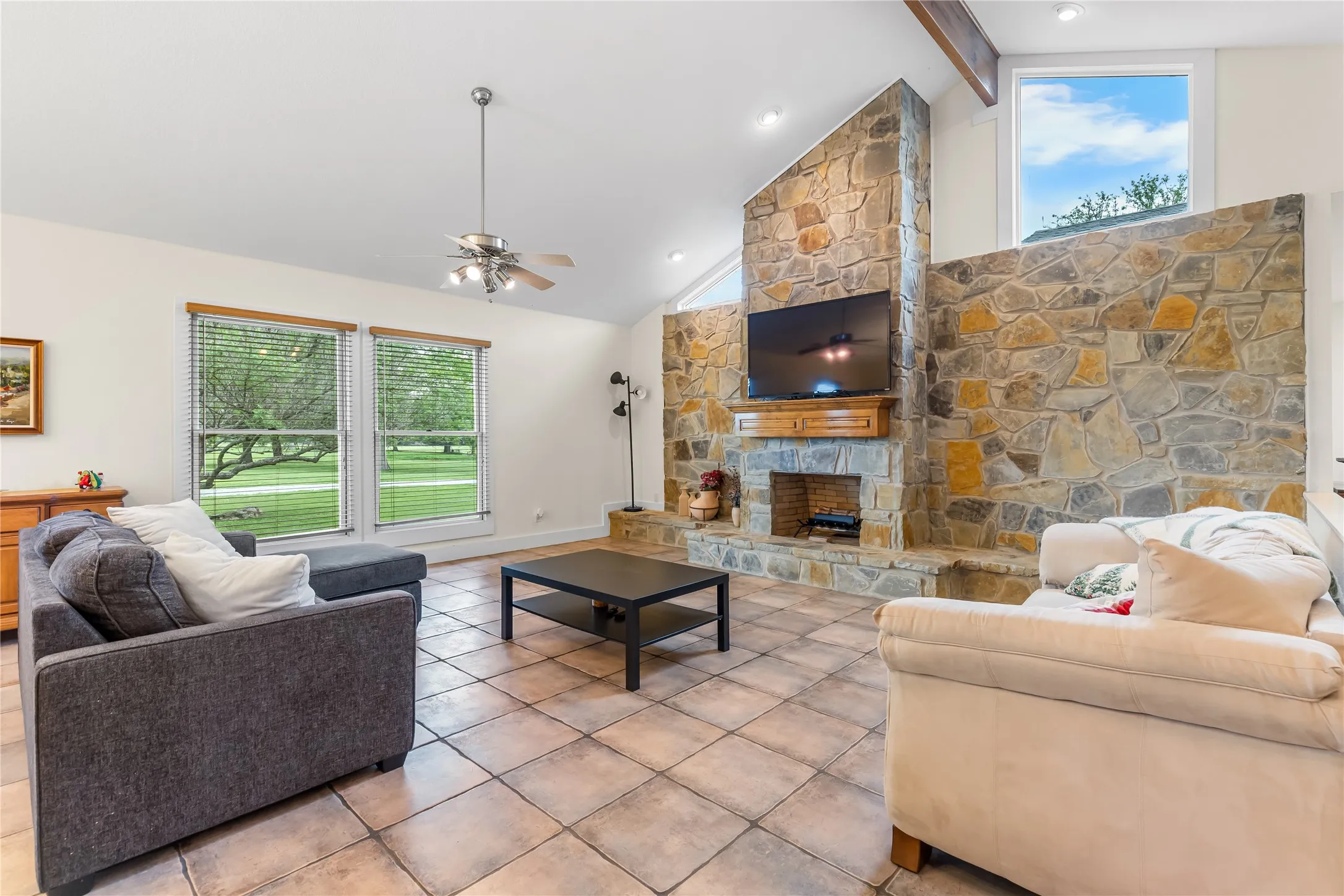 This living area features a natural stone fireplace, vaulted ceilings, and large windows offering views of the outdoors