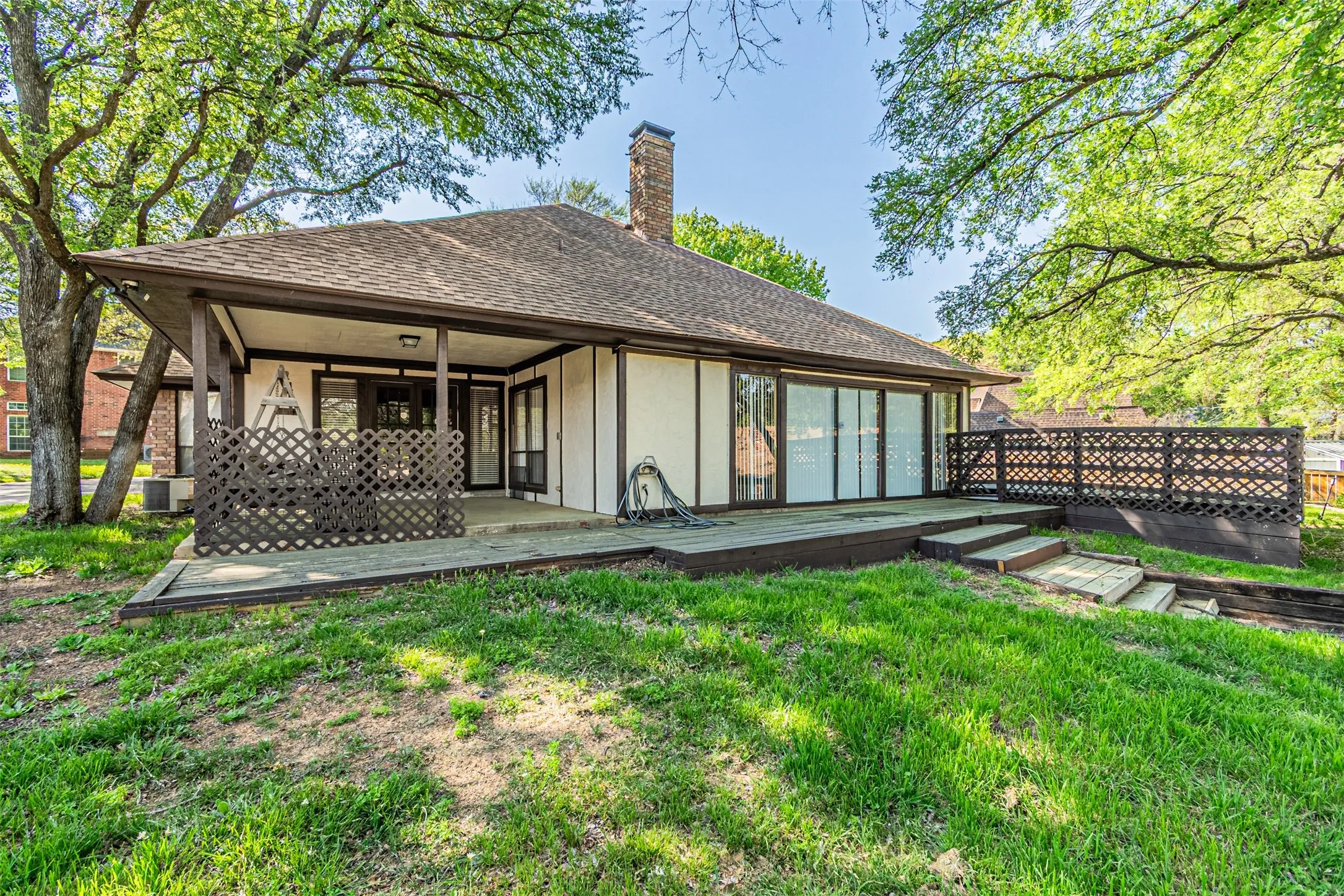 Back of property featuring a chimney, a deck, a lawn, stucco siding, and a shingled roof