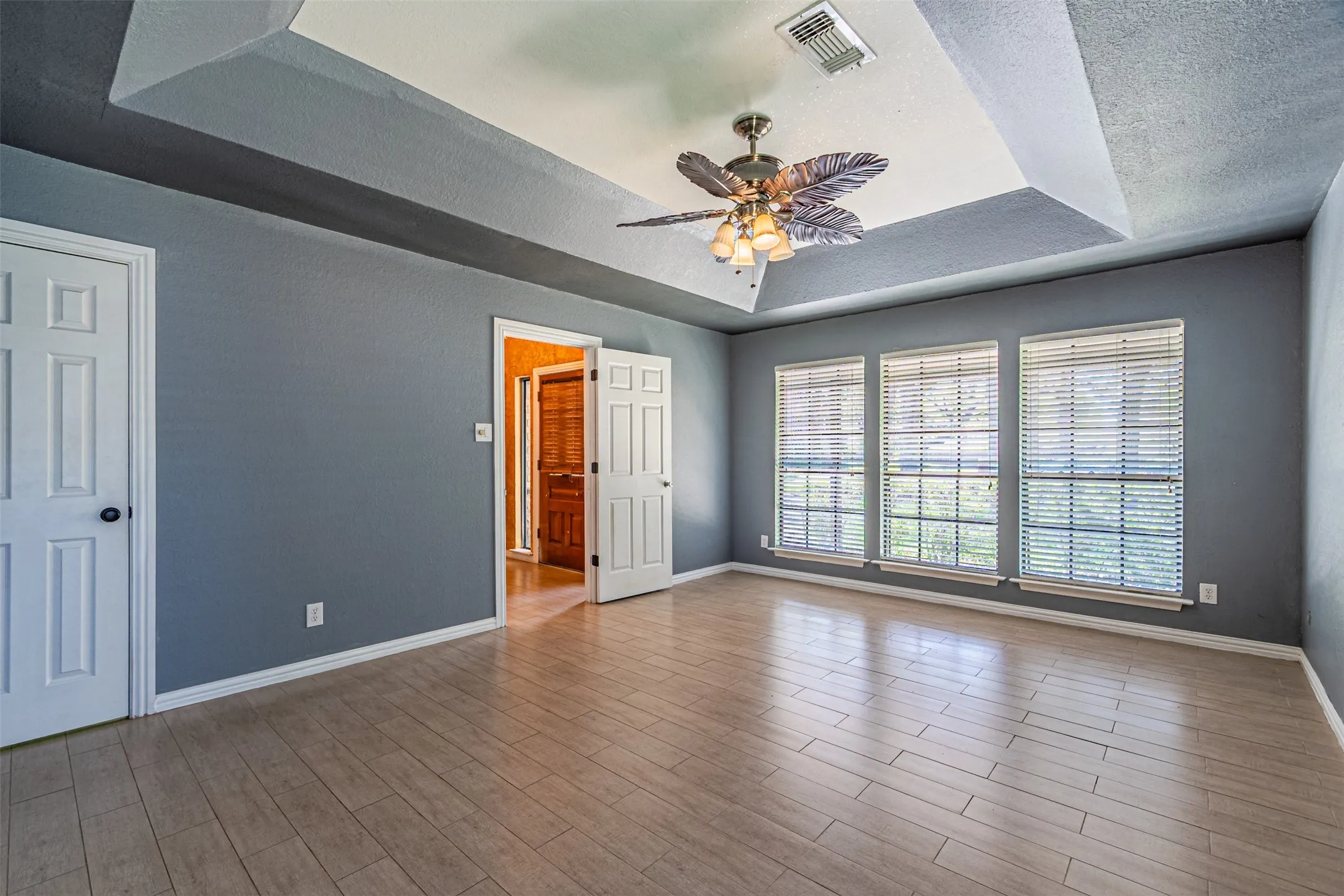 Unfurnished bedroom with a tray ceiling, a textured ceiling, ceiling fan, and dark wood-style floors
