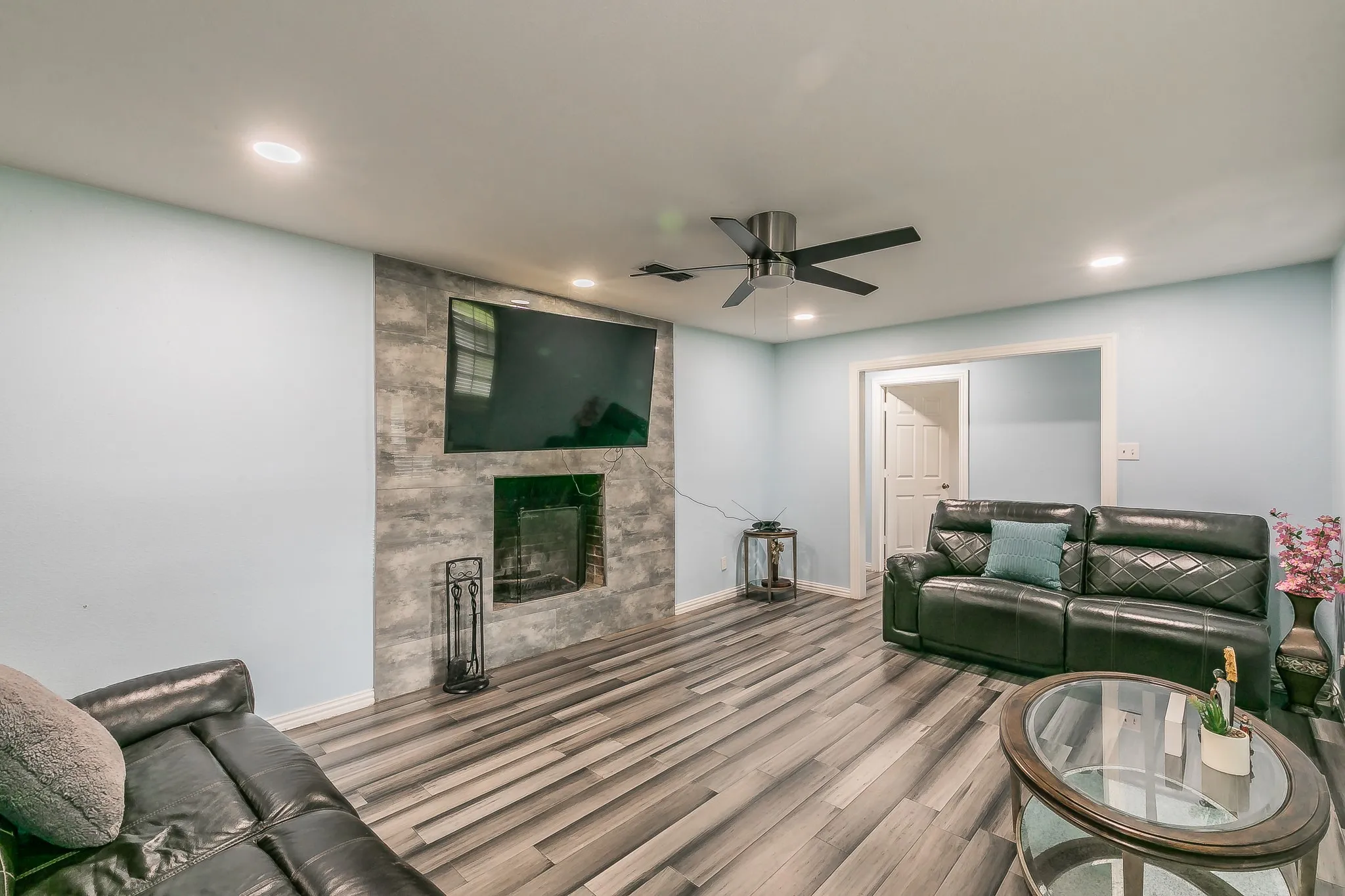 Living room with wood finished floors, ceiling fan, a large fireplace, and recessed lighting
