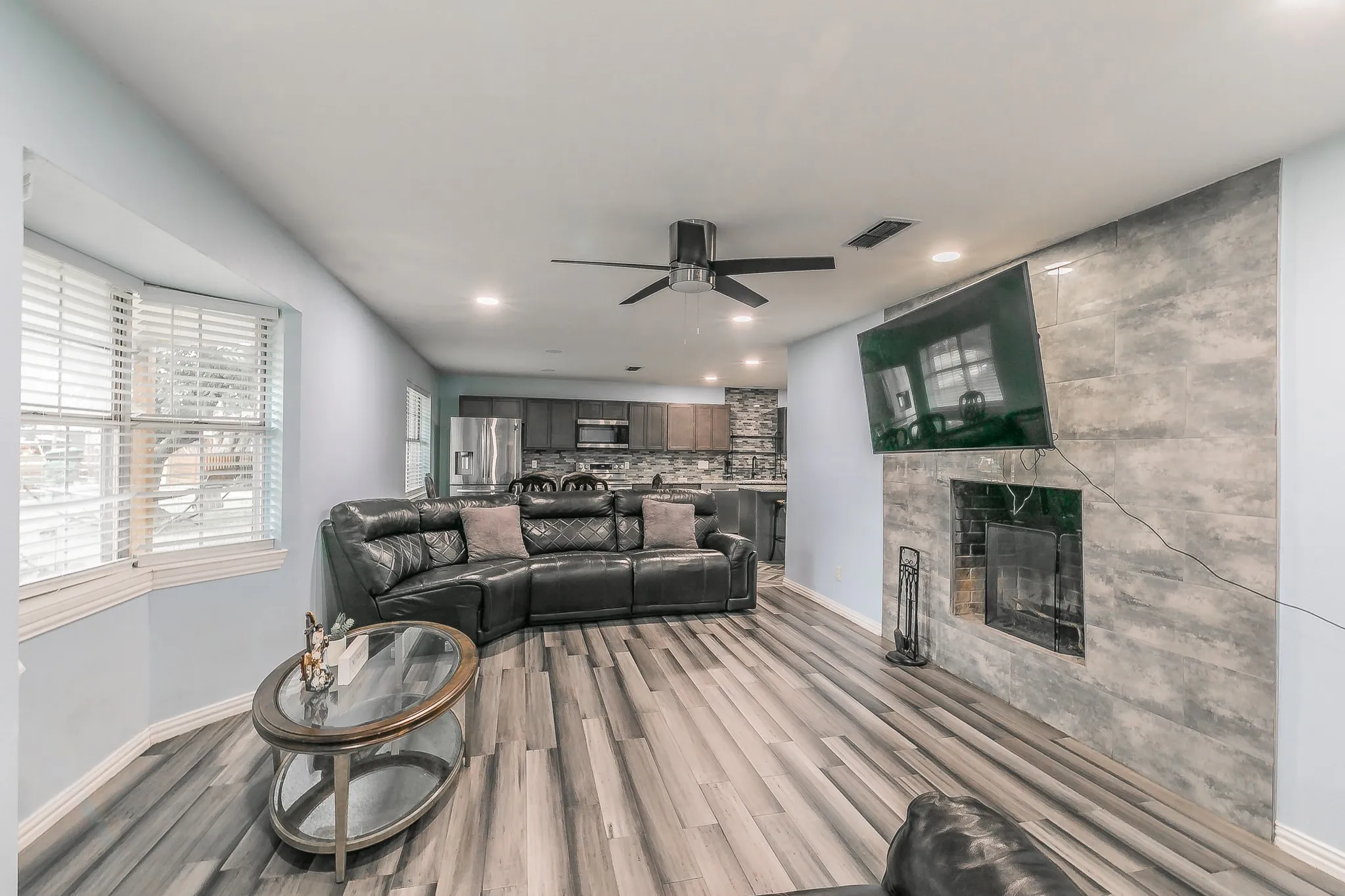 Living area with a ceiling fan, light wood-type flooring, a tile fireplace, and recessed lighting