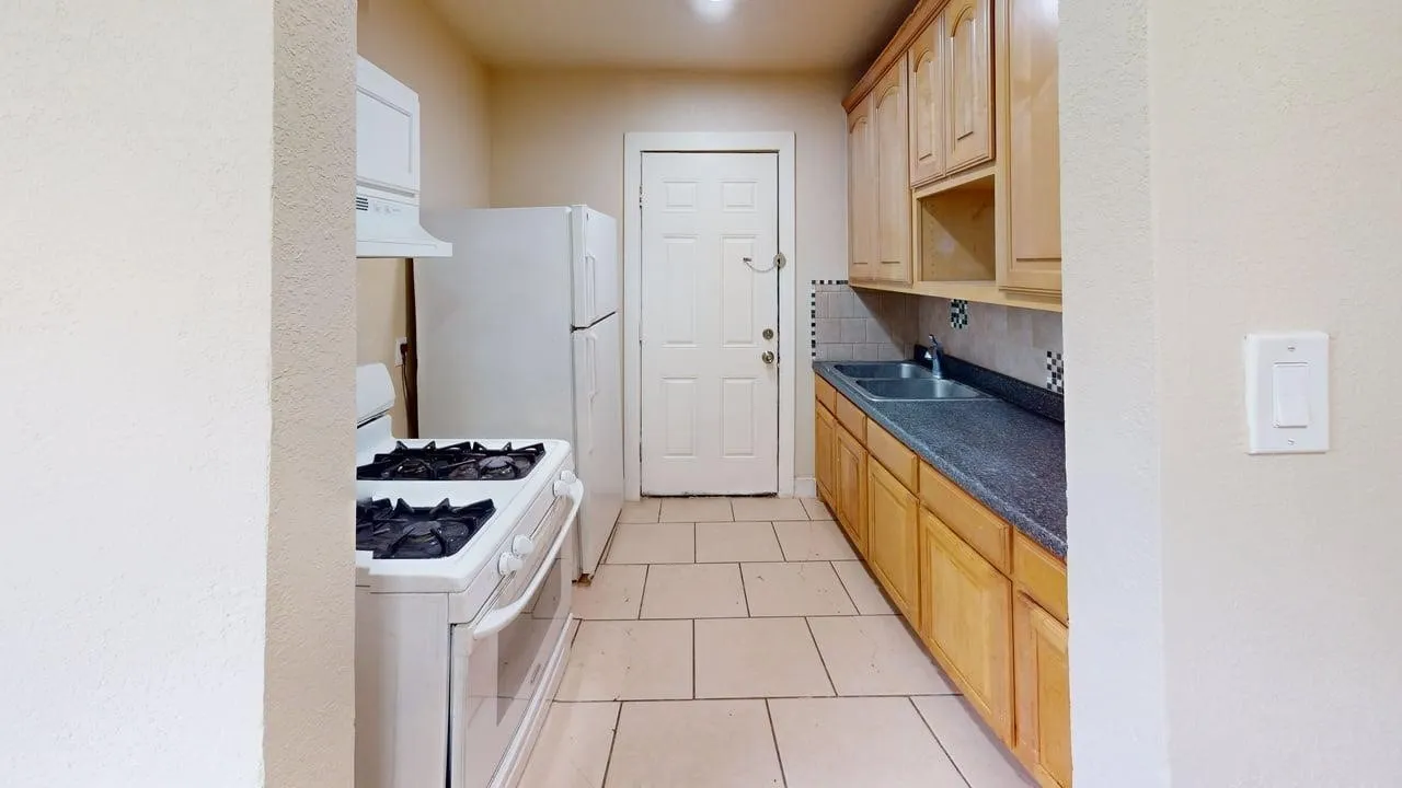 Kitchen with white range with gas stovetop, light wood finish cabinets, dark countertops, backsplash, and light tile patterned floors