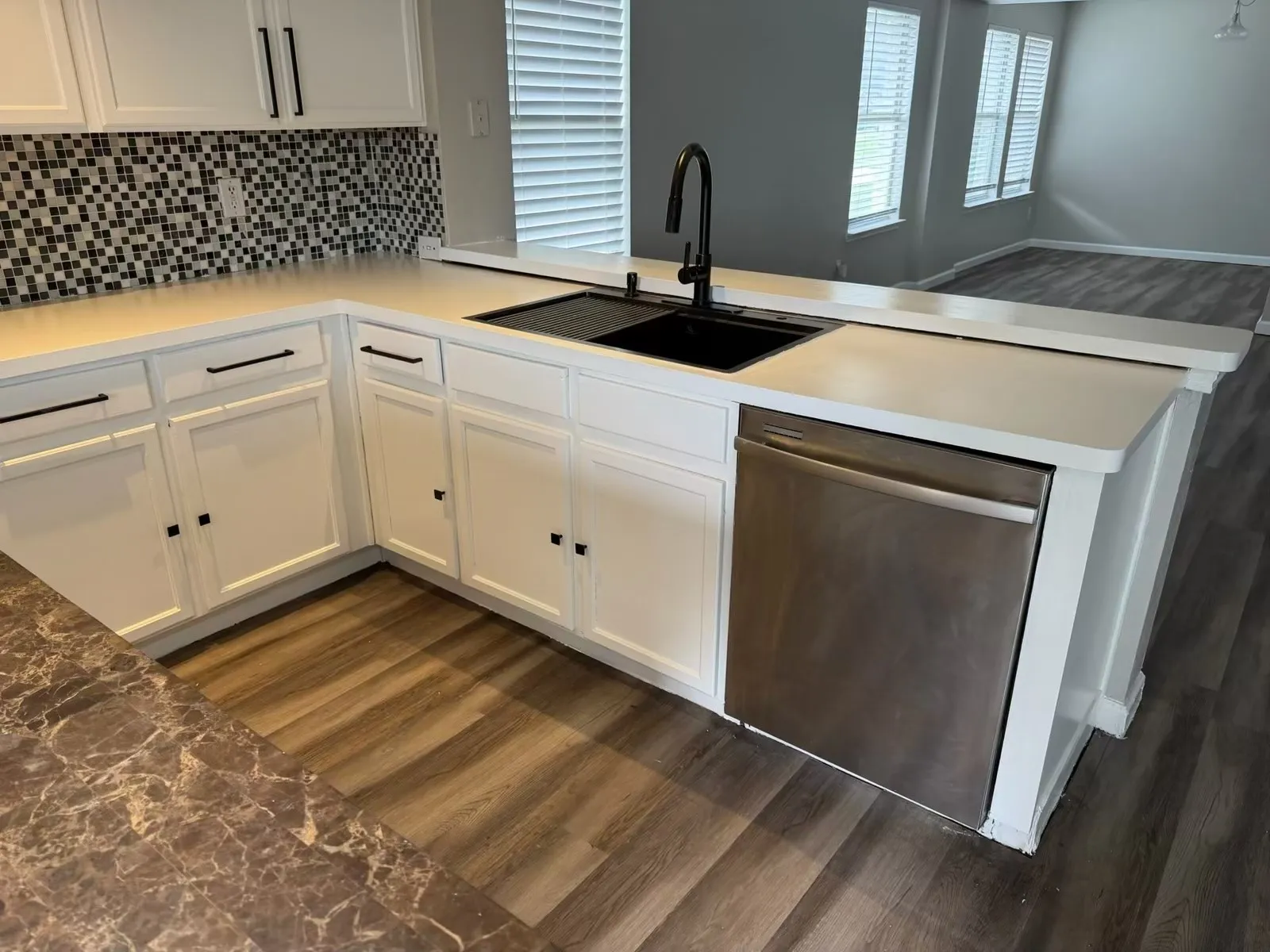 Modern kitchen featuring white cabinetry, a black square sink with a gooseneck faucet, light-toned countertops, a mosaic tile backsplash, and wood-finish flooring