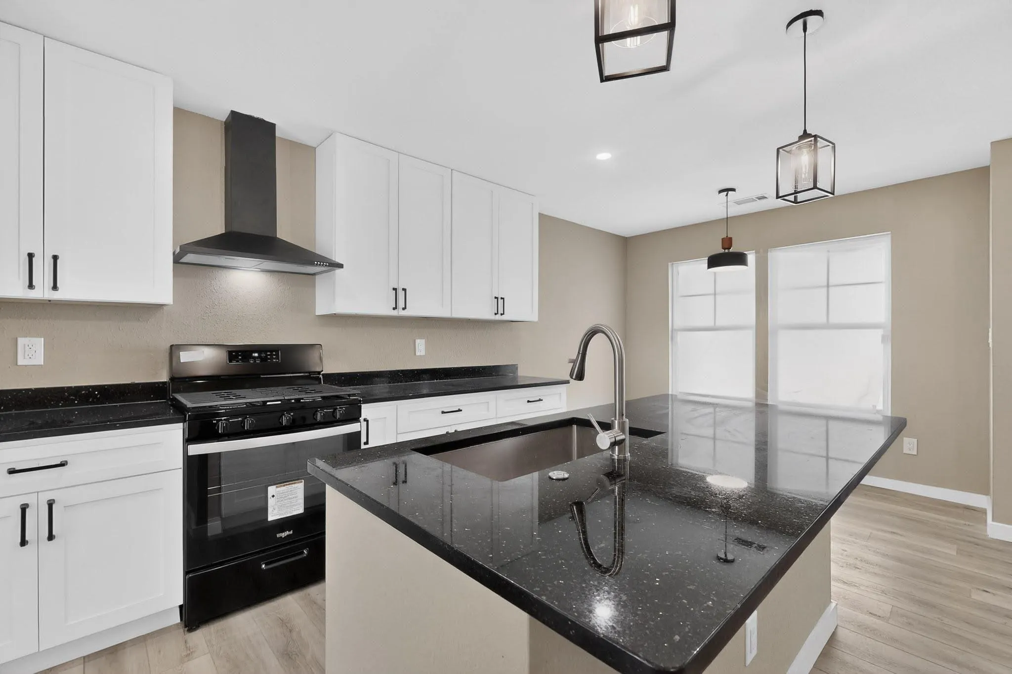 Kitchen featuring black range with gas cooktop, light wood-type flooring, white cabinets, and a center island with sink