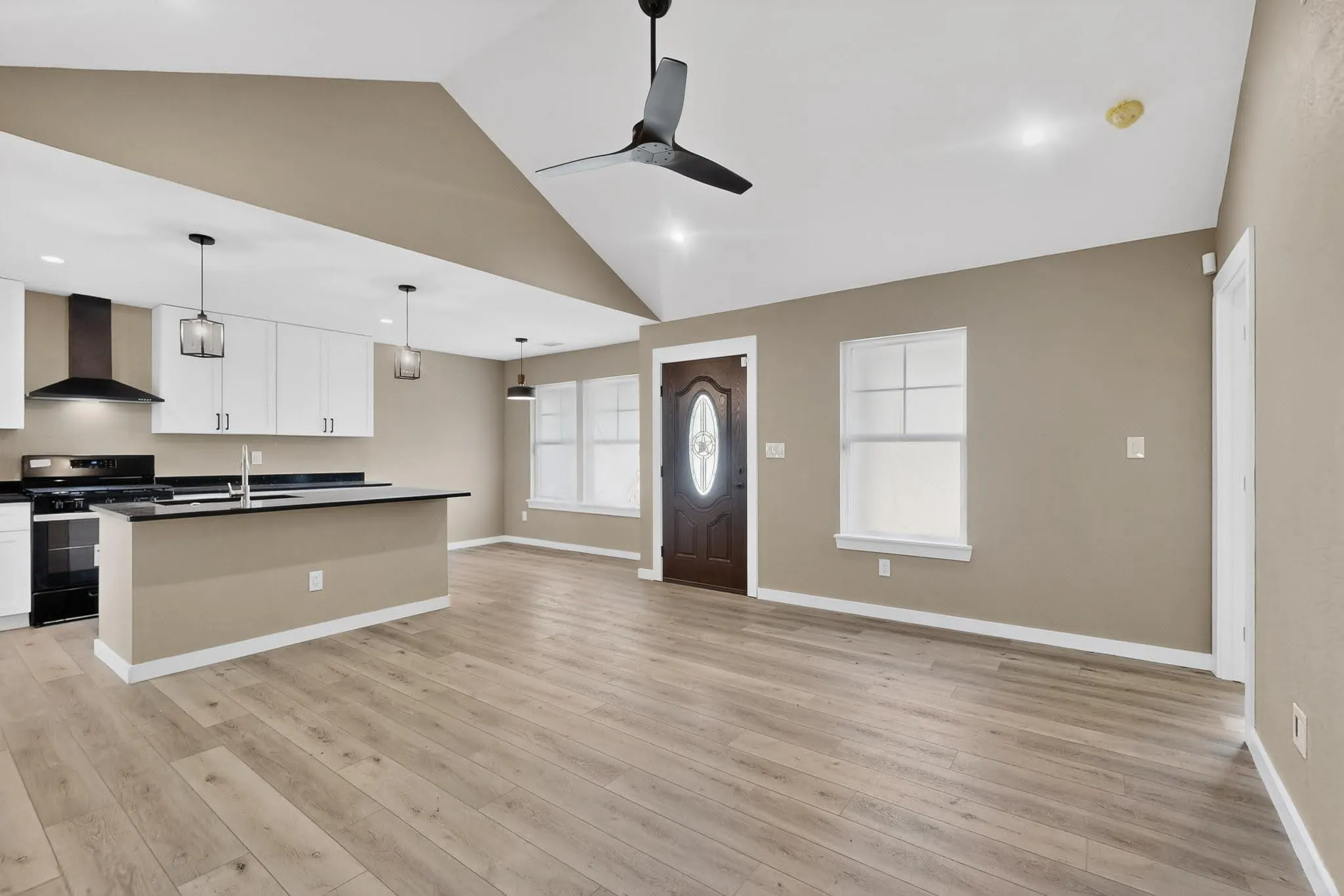 Kitchen with dark countertops, open floor plan, a center island with sink, gas stove, and pendant lighting
