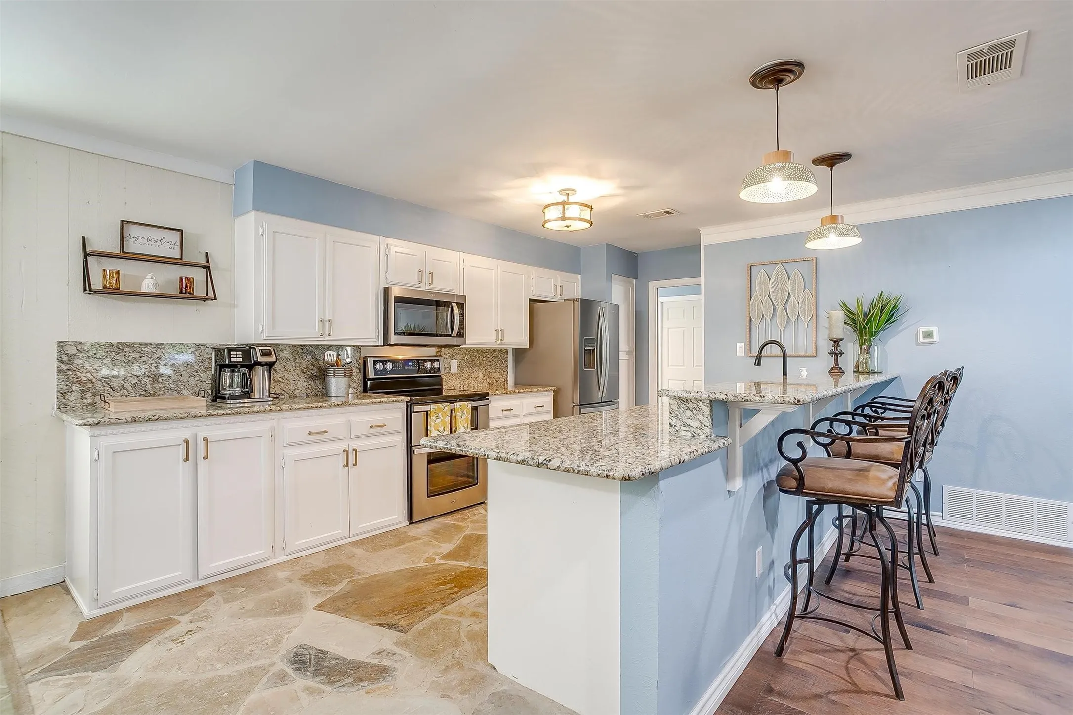 Kitchen with white cabinets, stainless steel appliances, light granite counters, a kitchen bar, and decorative light fixtures