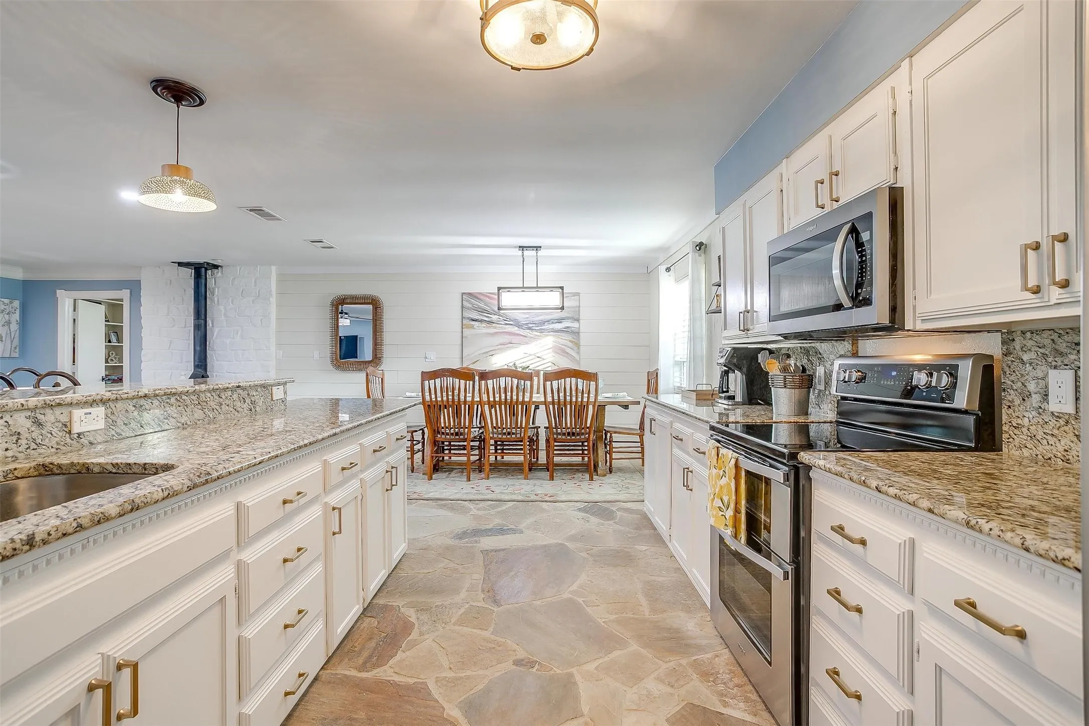 Kitchen with stainless steel appliances, stone flooring, light granite counters, and white cabinets