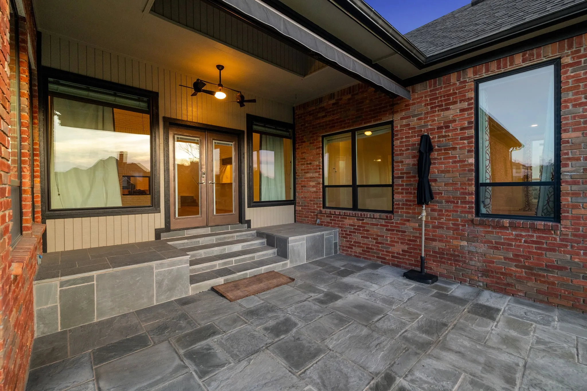 Doorway to property featuring french doors, a patio, a ceiling fan, brick siding, and a shingled roof