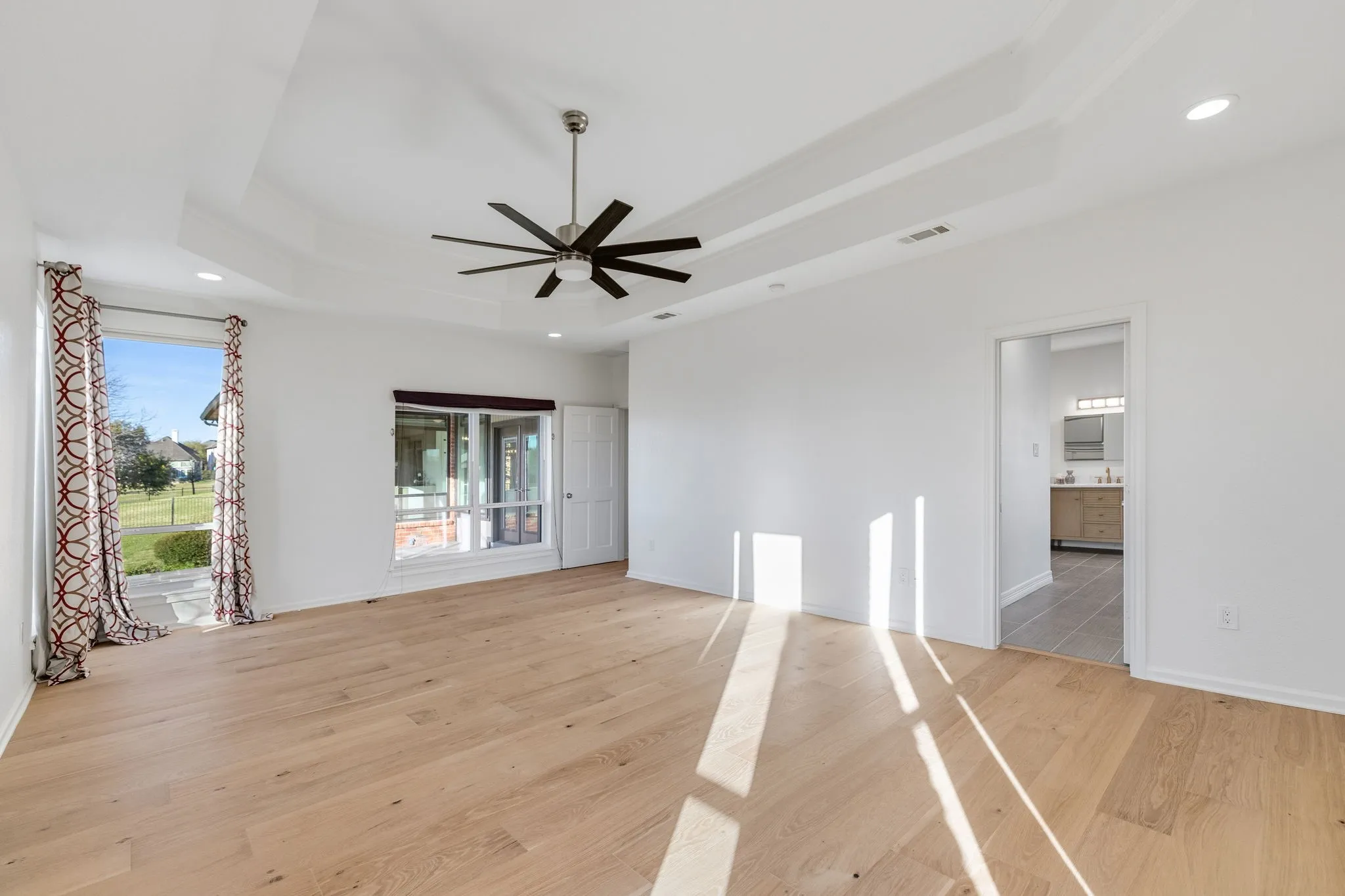 Unfurnished living room featuring light wood-style flooring, a ceiling fan, recessed lighting, and a tray ceiling
