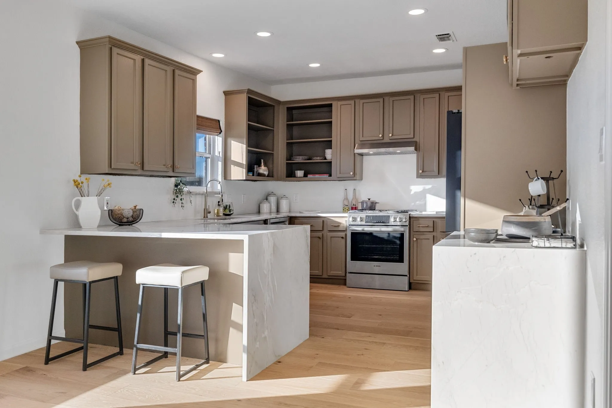 Kitchen with a peninsula, stainless steel range, a kitchen bar, open shelves, and light wood-type flooring