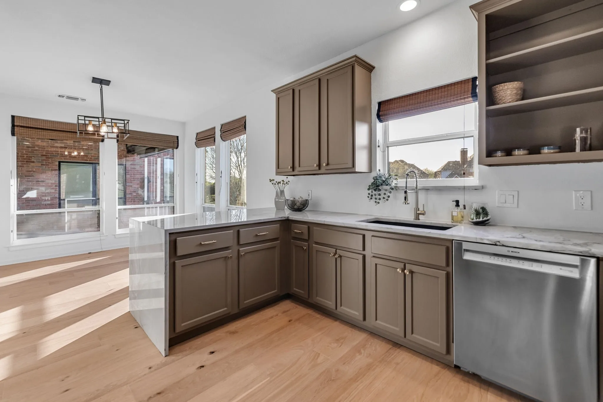 Kitchen with a peninsula, dishwasher, light stone counters, and light wood-style flooring