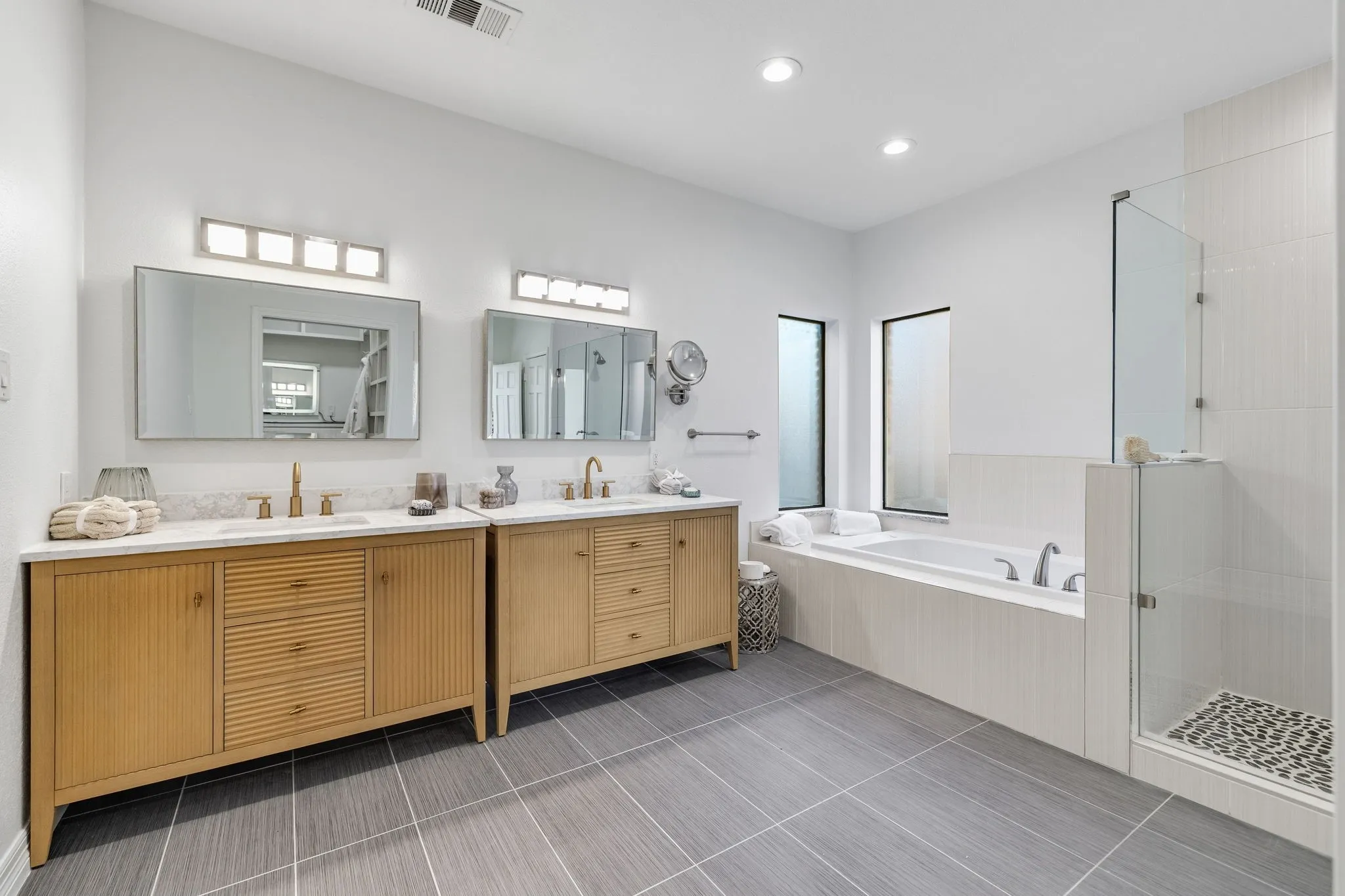 Full bathroom with two vanities, a shower stall, a garden tub, dark tile patterned floors, and recessed lighting