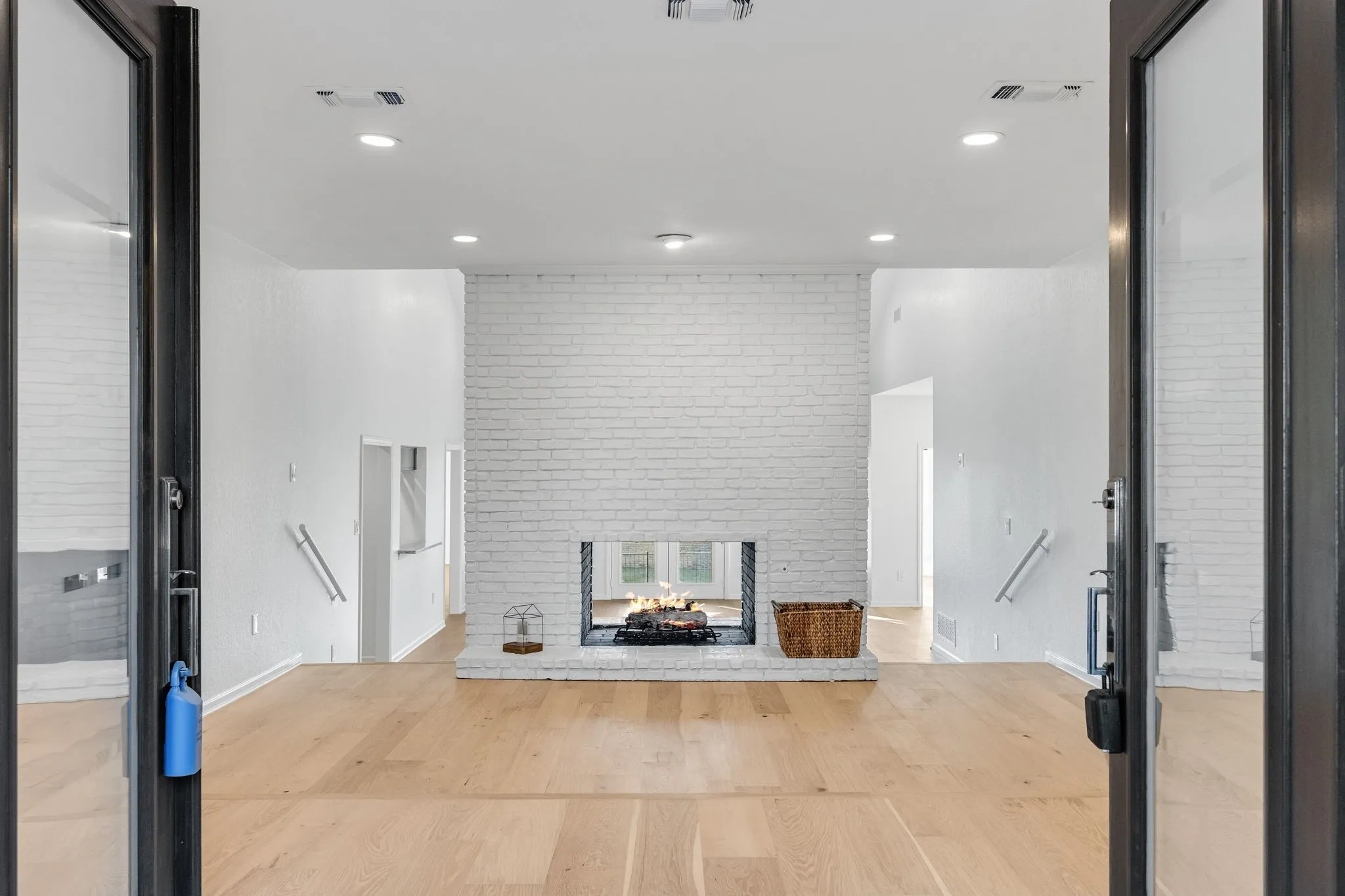 Unfurnished living room featuring light wood-style flooring, a fireplace, brick wall, and recessed lighting