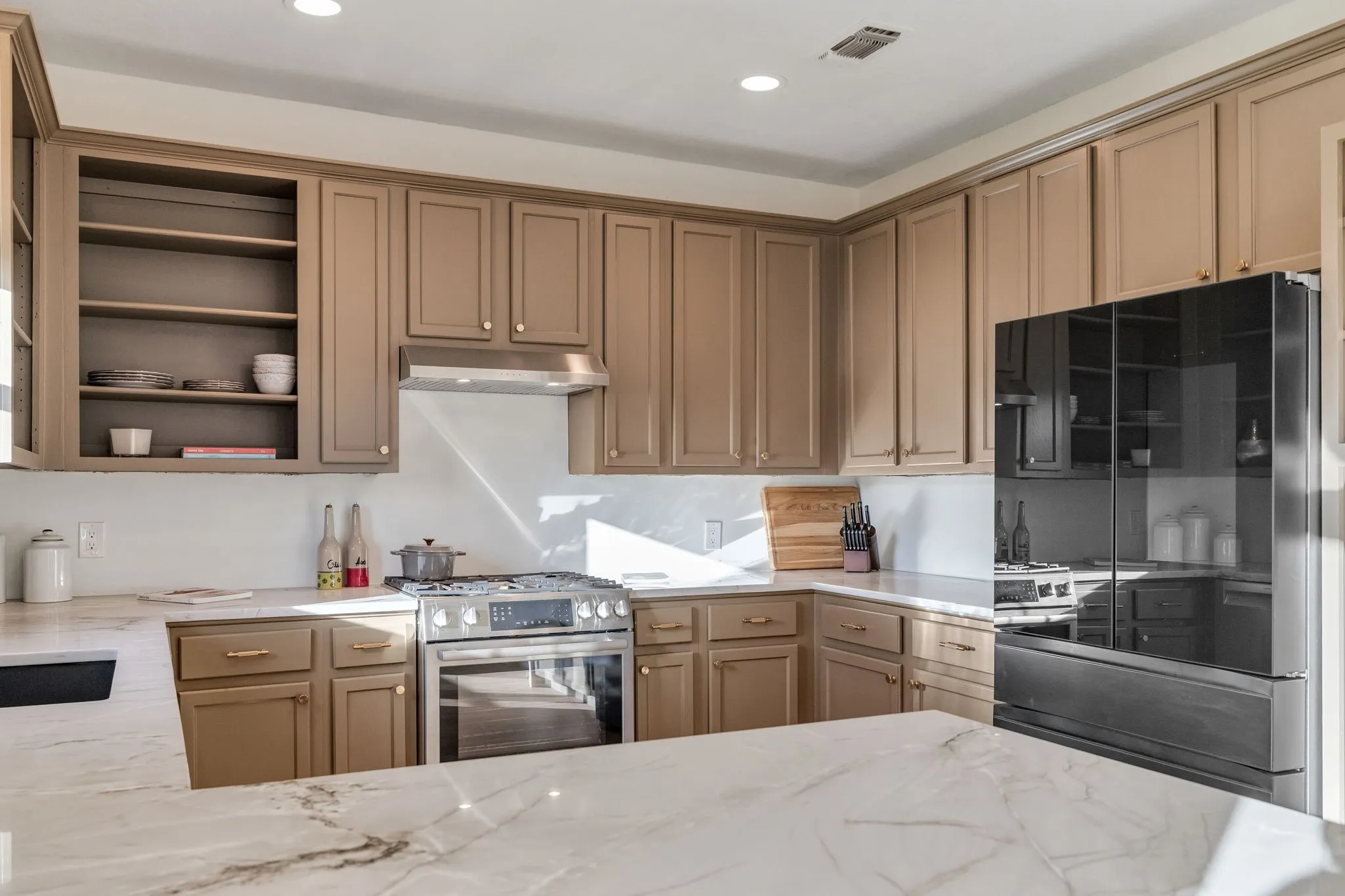 Kitchen featuring open shelves, stainless steel range with gas stovetop, freestanding refrigerator, light stone countertops, and recessed lighting
