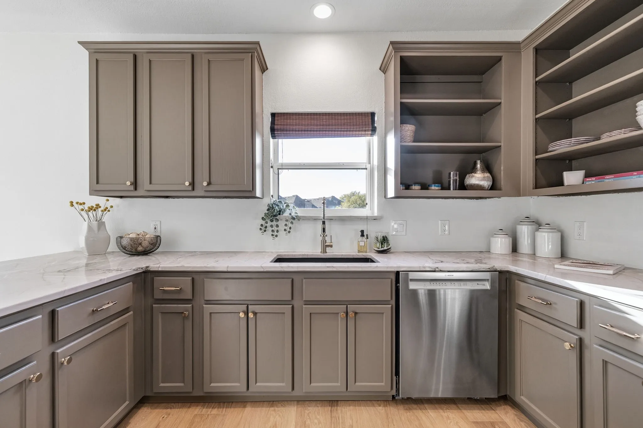 Kitchen with light stone counters, stainless steel dishwasher, open shelves, and gray cabinets